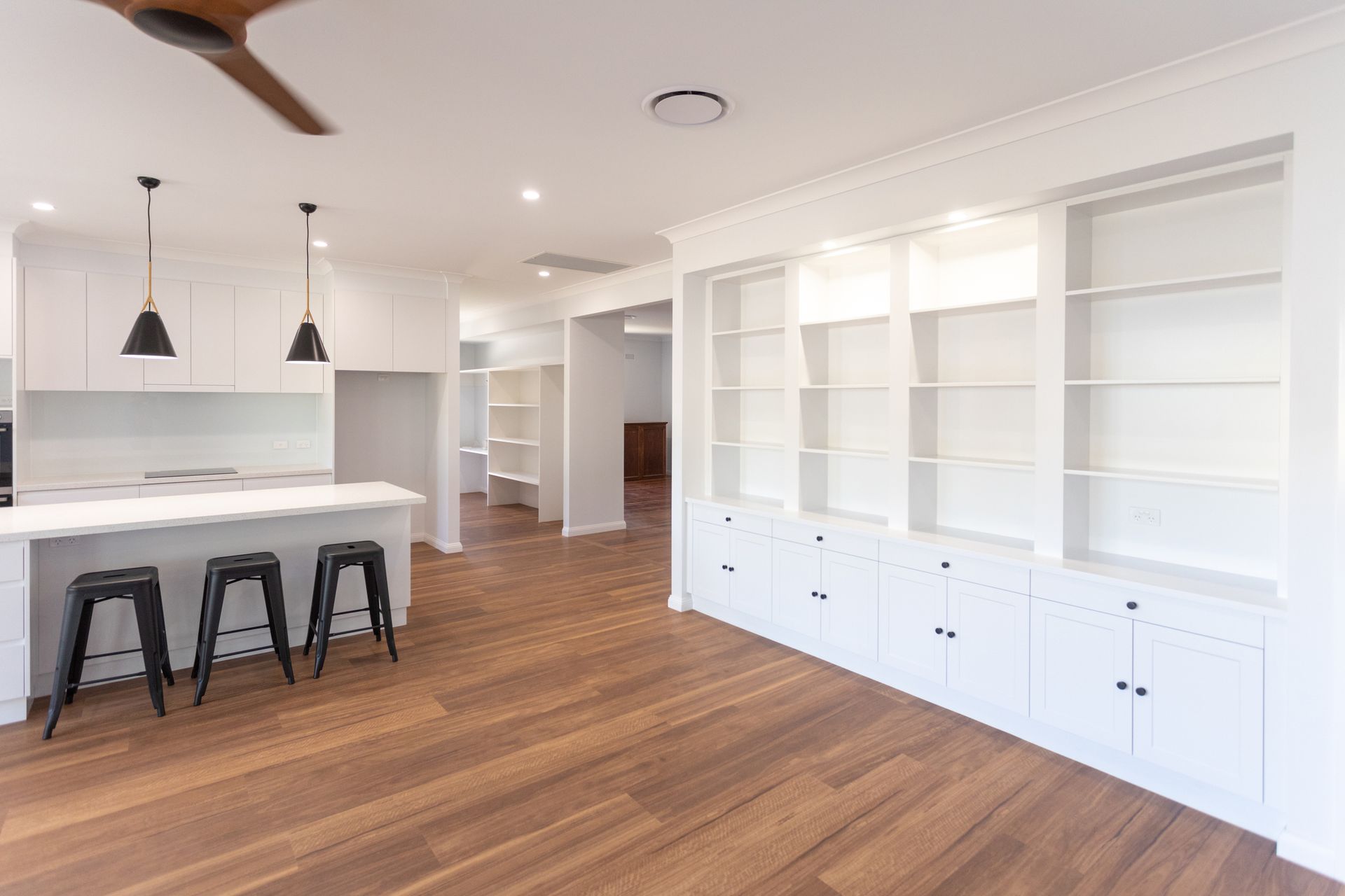 A kitchen with white cabinets and wooden floors and a ceiling fan.
