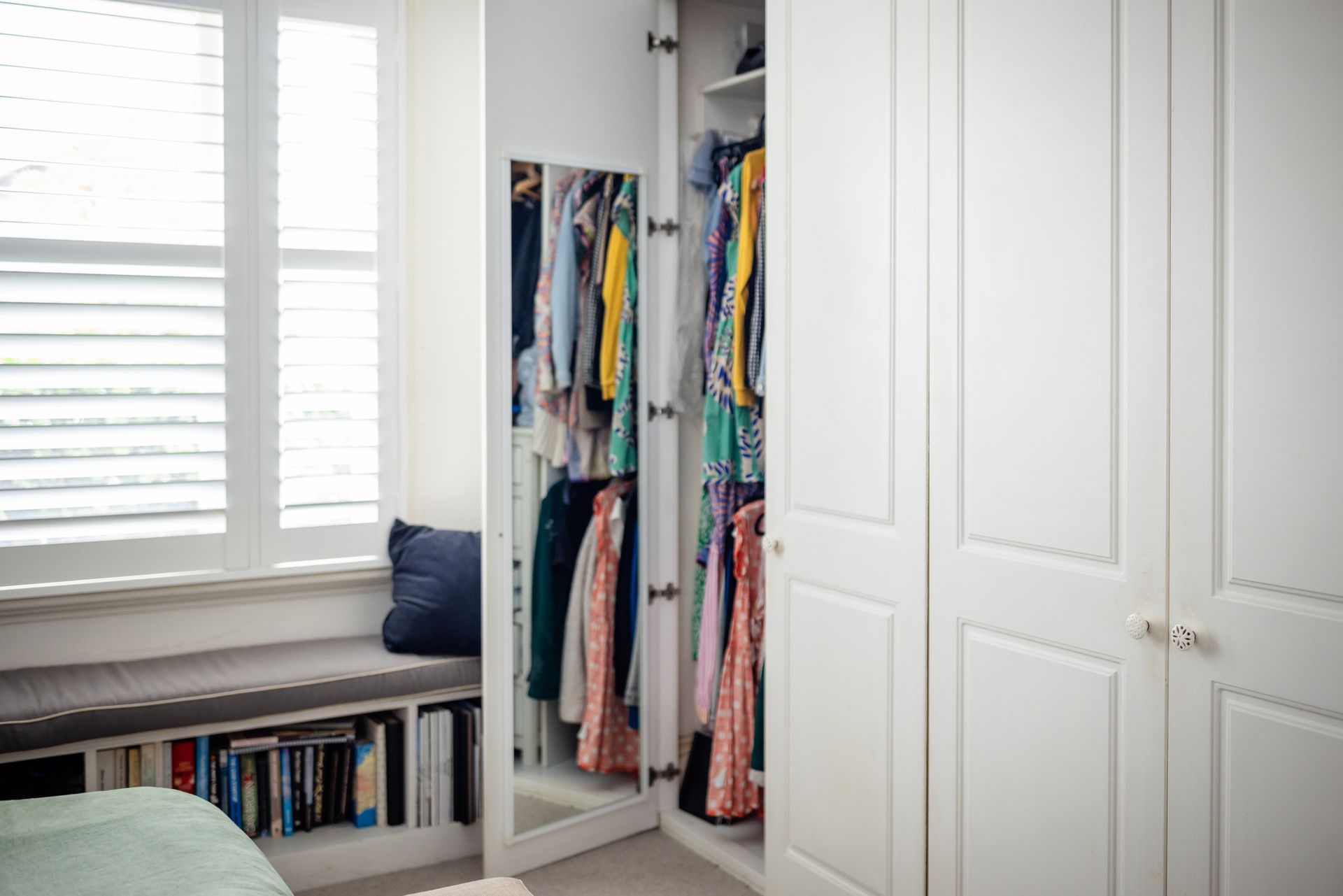 A walk in closet with a window seat and a mirror.