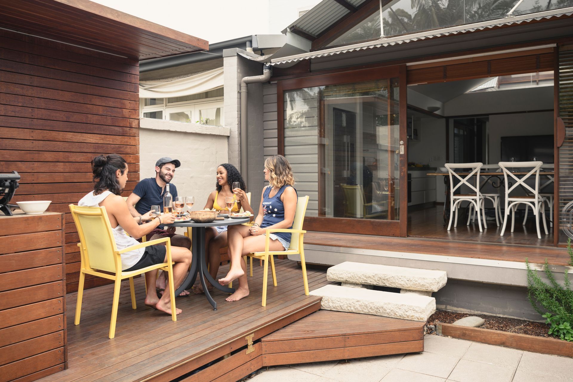 A group of people are sitting at a table on a deck in front of a house.