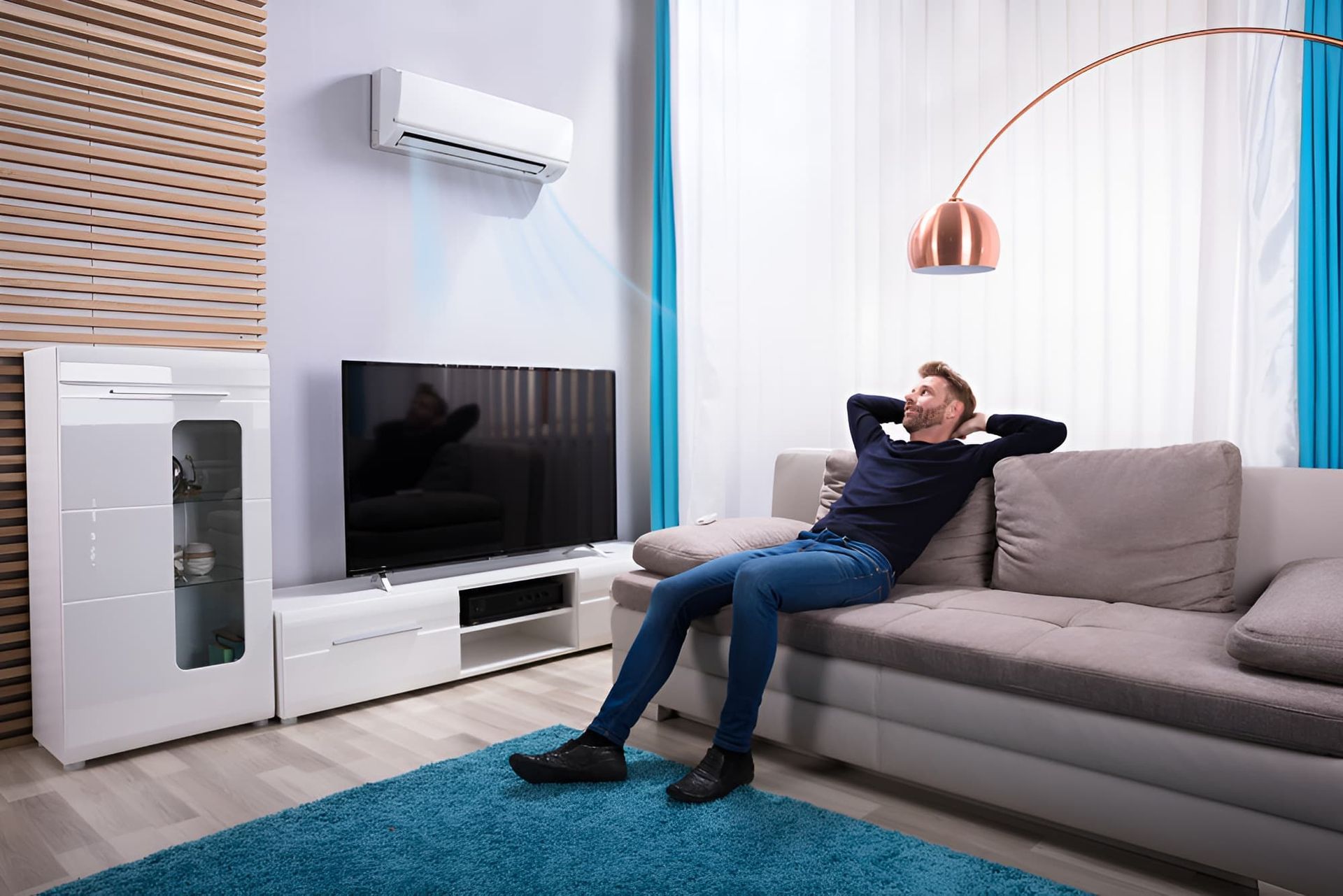 A Man is Sitting on a Couch in a Living Room With a Television and Air Conditioner — Beards Refrigeration & Air Conditioning in Marian, QLD