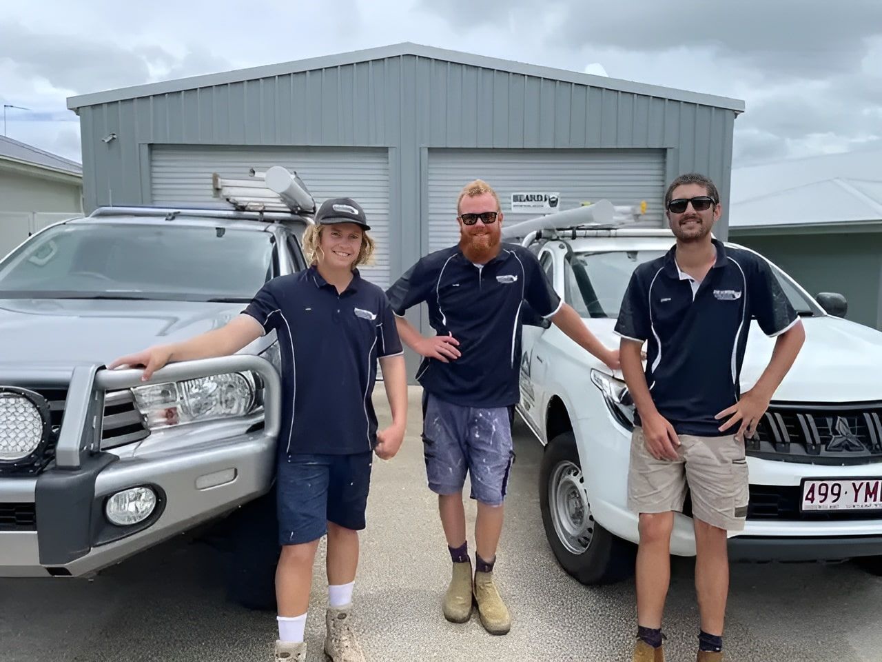 Three Men Are Standing Next to Two Trucks in Front of a Garage — Beards Refrigeration & Air Conditioning in Marian, QLD