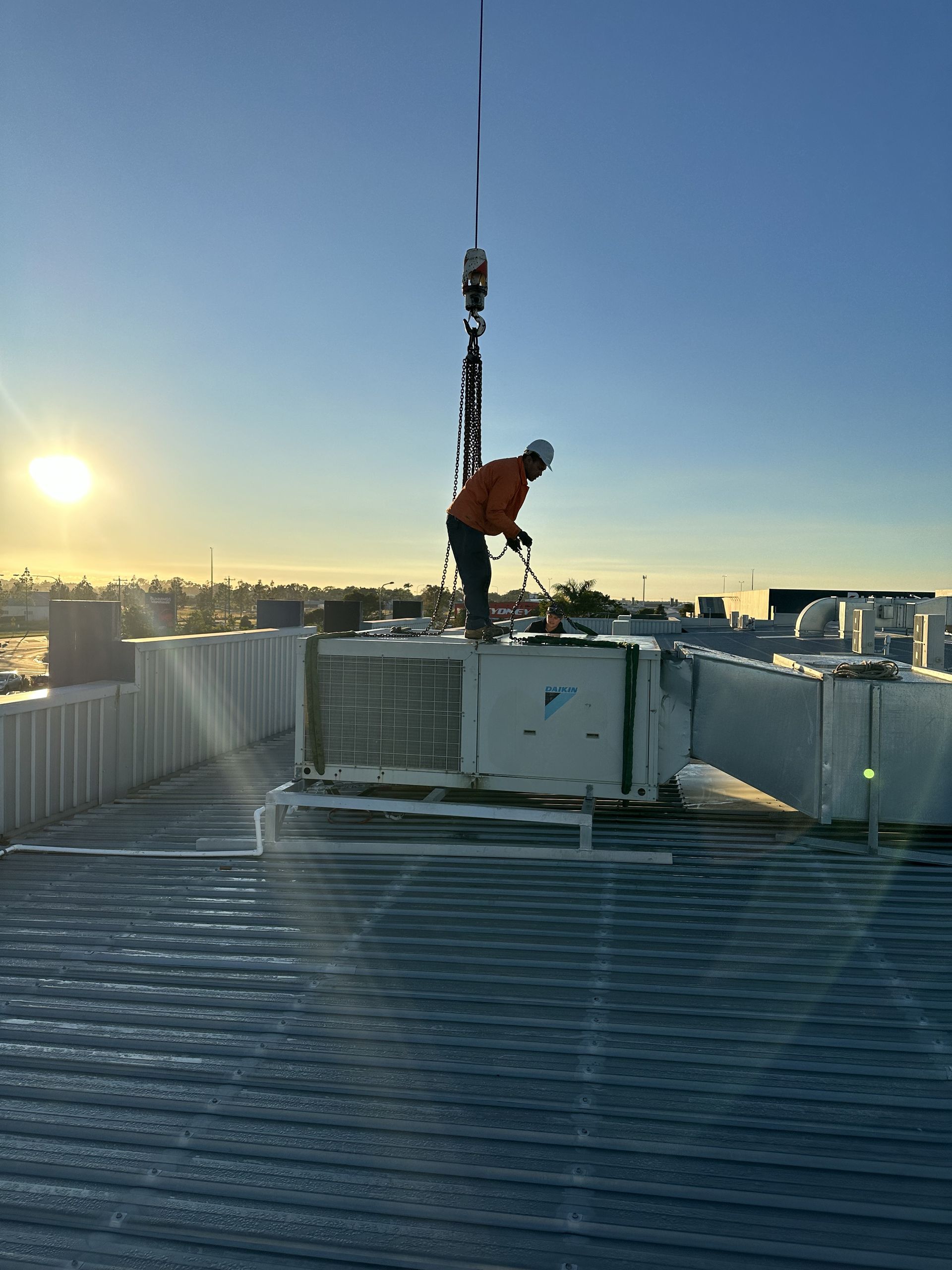 A Man Is Holding A Couple Of Gauges In His Hands In Front Of An Air Conditioner — Beards Refrigeration & Air Conditioning in Marian, QLD