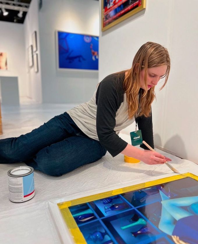 A woman is kneeling on the floor painting a frame