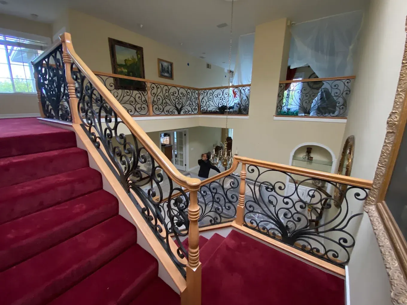 Red carpet staircase with decorative black ironwork railing and wooden handrails in a two-story home.