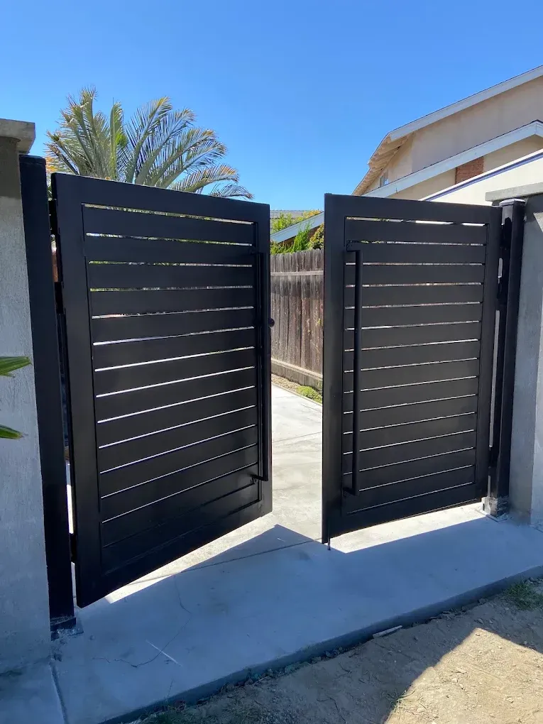 Black, horizontal-slat gate, open, revealing a driveway and a blue sky.