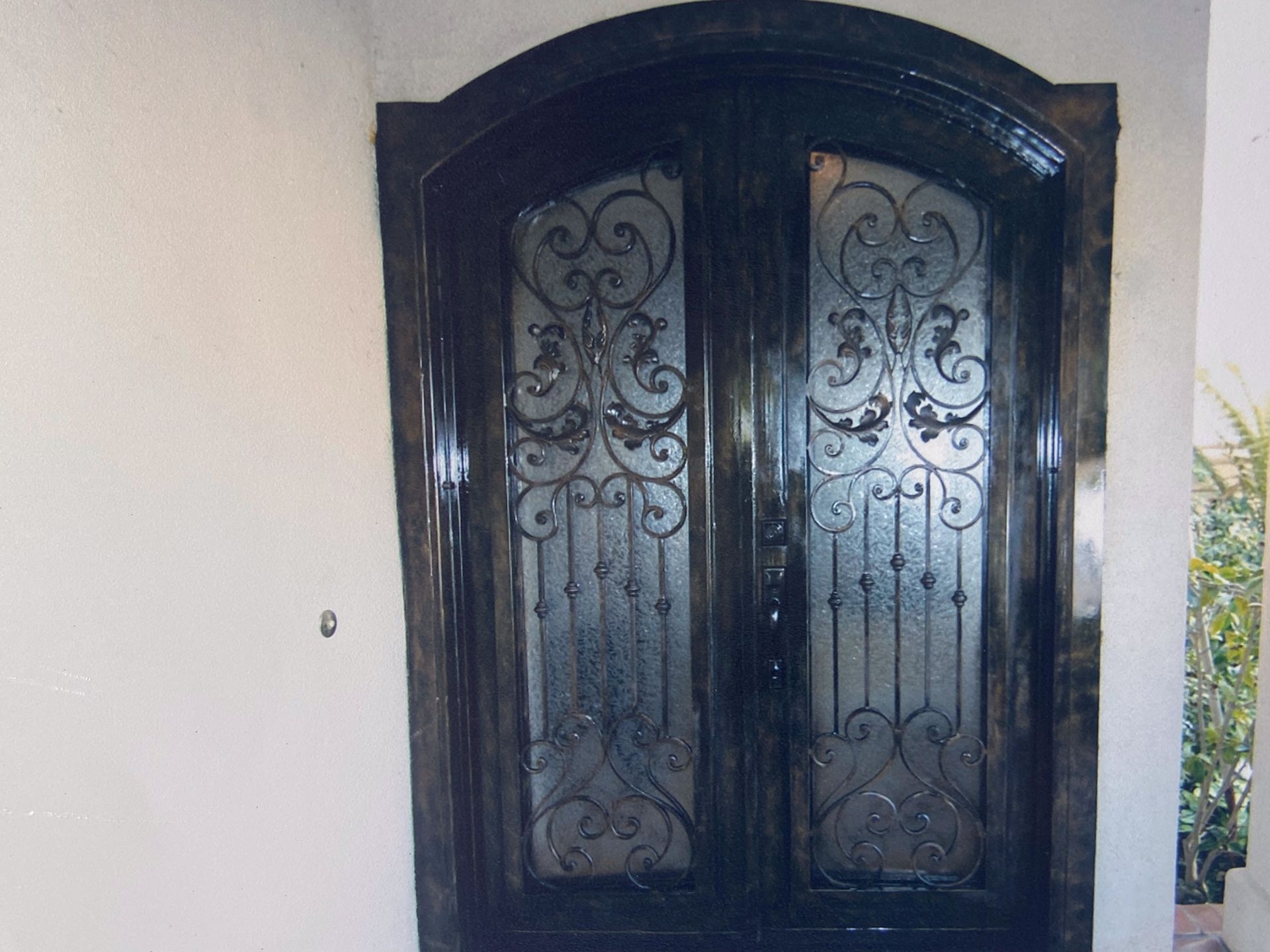 Dark wooden double front doors with ornate wrought iron and arched glass panels.