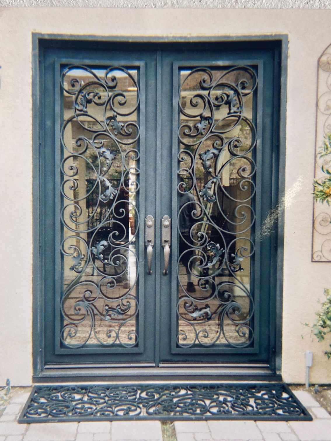 Dark blue double front doors with ornate wrought iron and glass panels. A decorative doormat sits below.