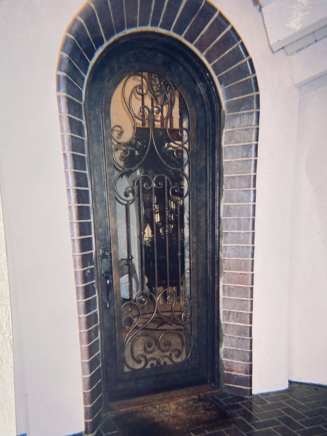 Ornate iron door within a brick archway, on a tiled floor, inside a white-walled room.