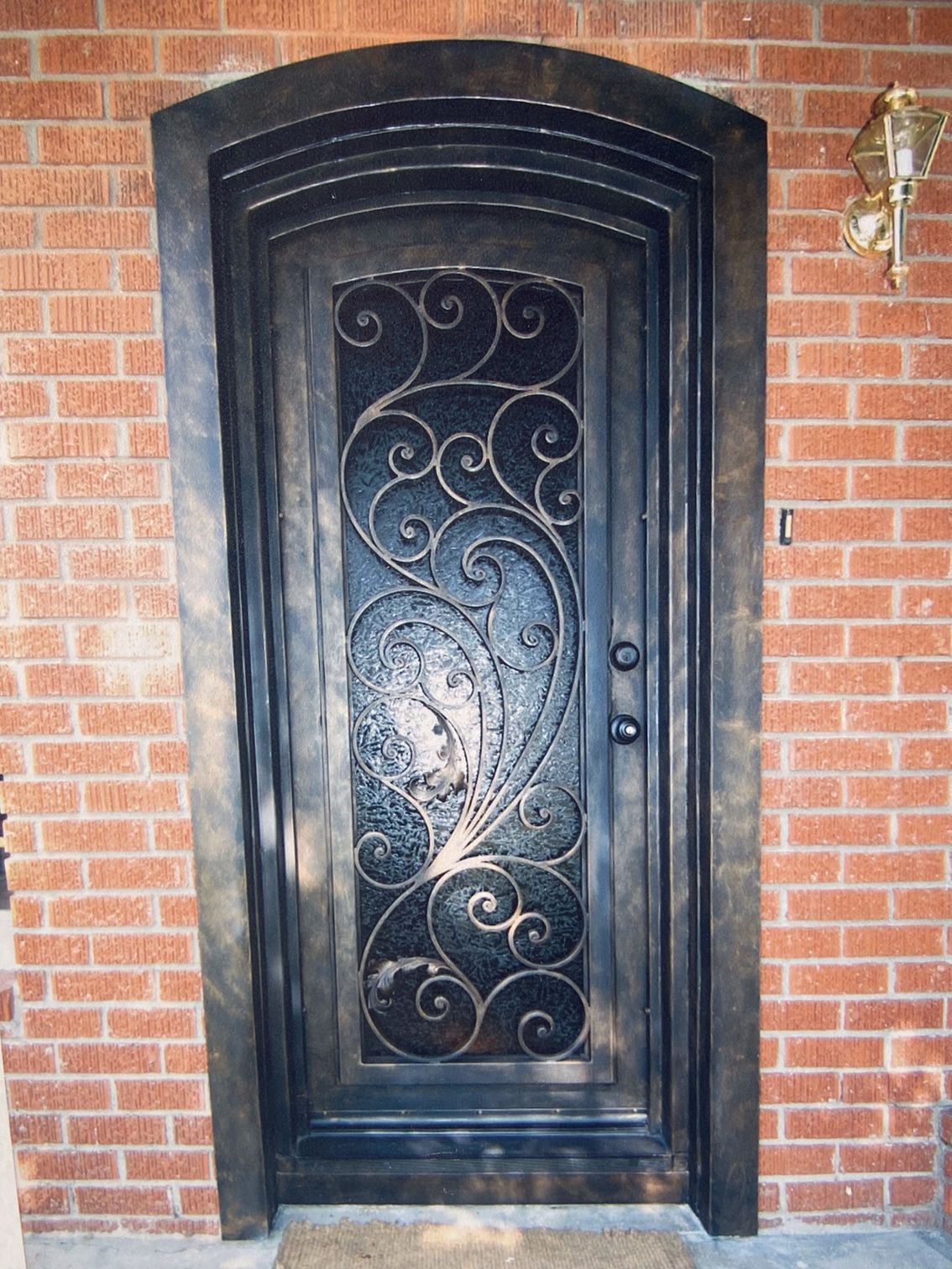 Ornate black iron front door with scrollwork, set in a brick wall.