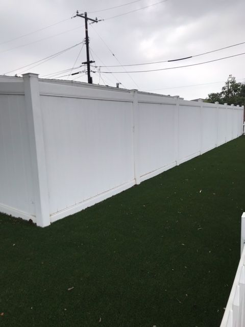 White privacy fence on green turf, under a cloudy sky.