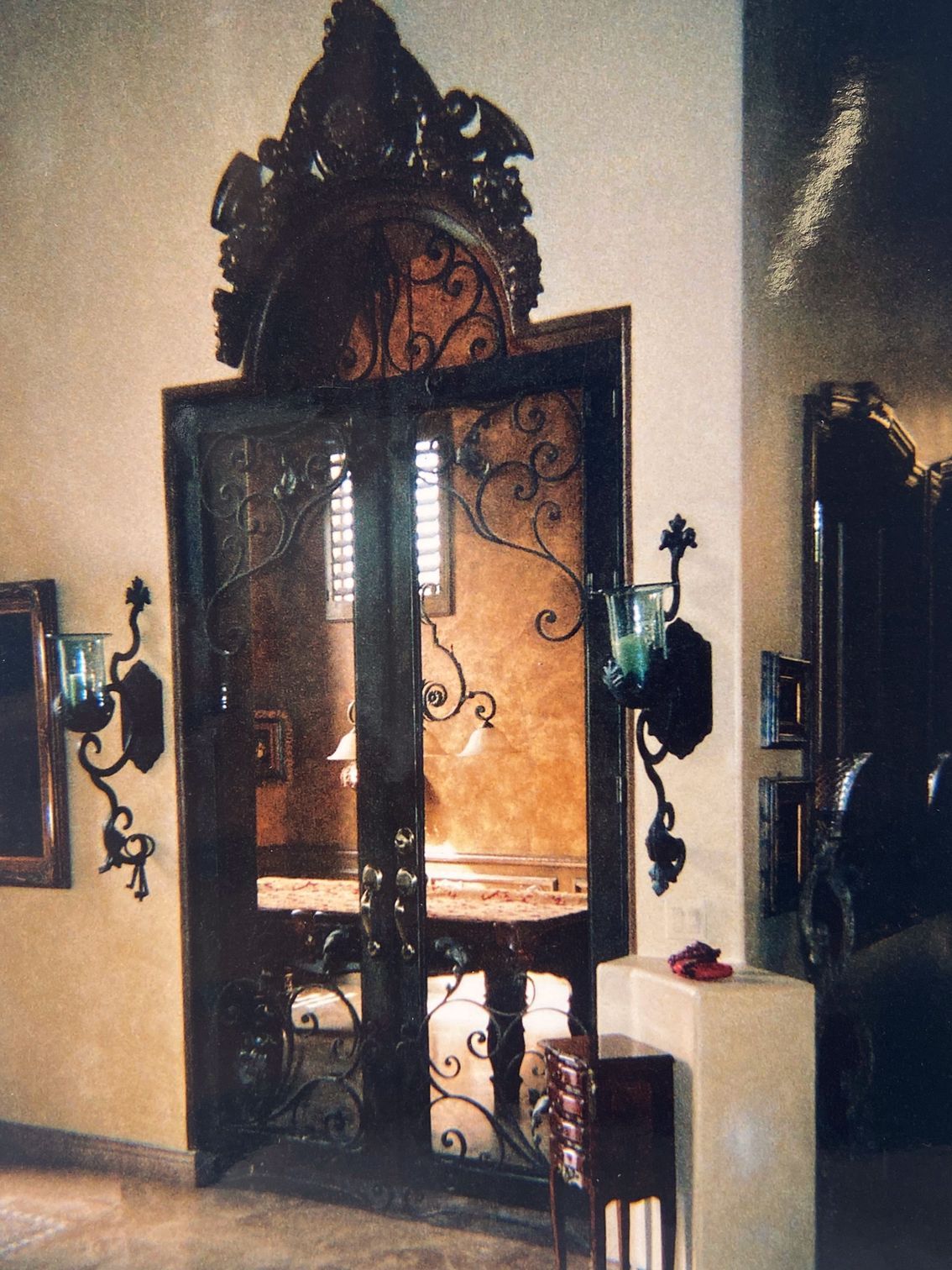Ornate wrought iron double doors with an elaborate top piece and sconces.