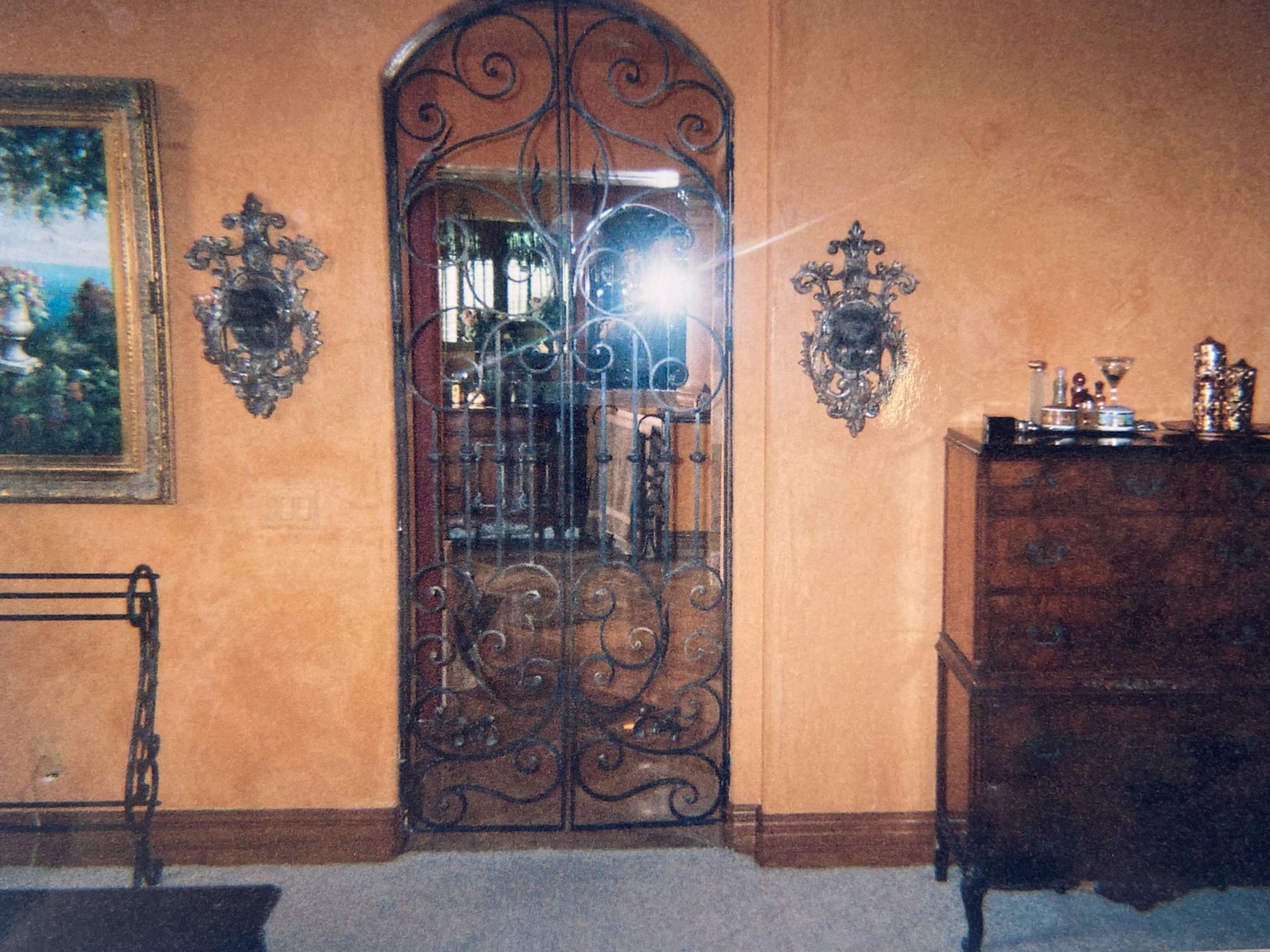 Ornate wrought-iron gate in a doorway, flanked by decorative wall sconces and a cabinet.