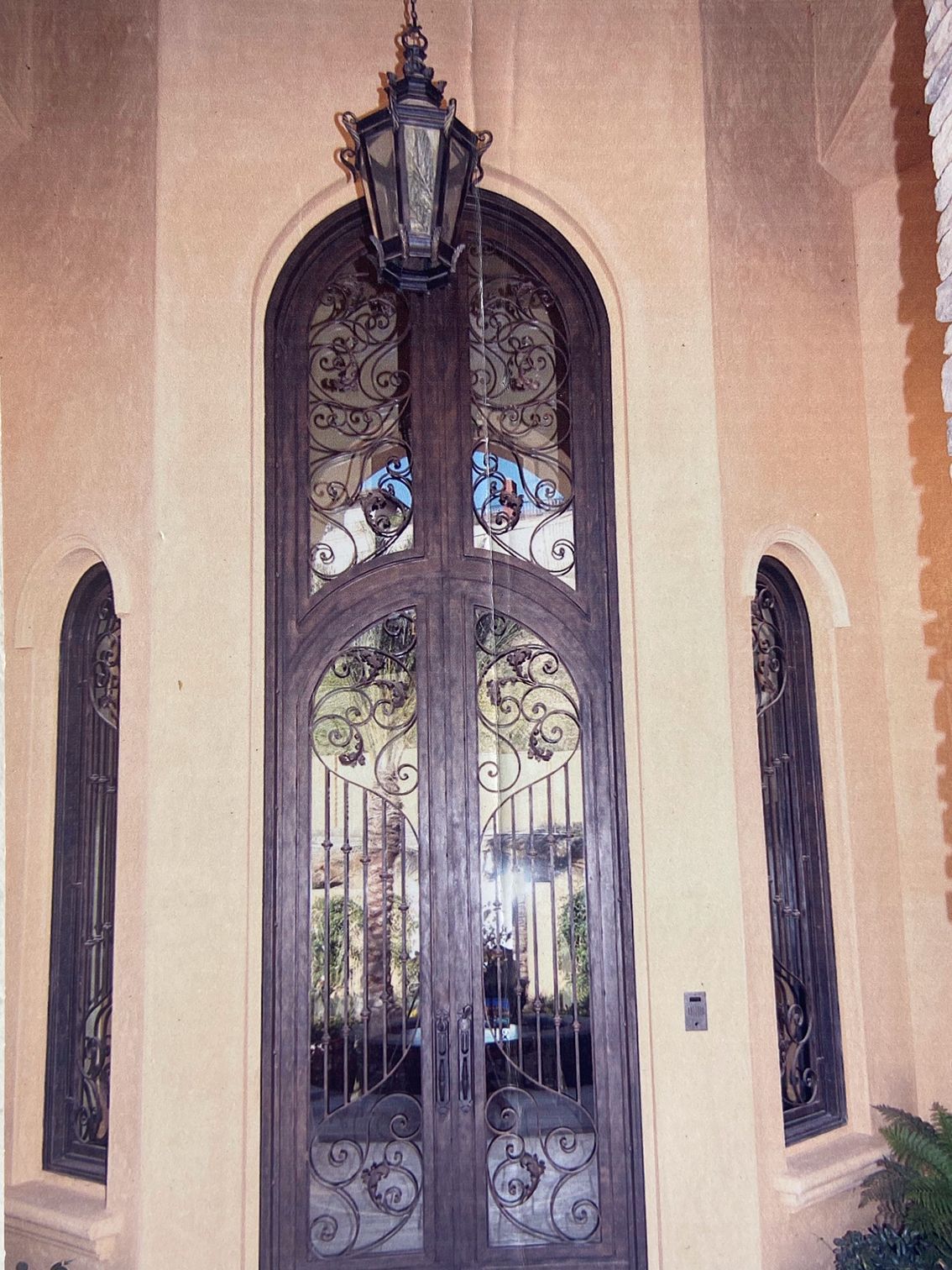 Ornate double doors with ironwork and arched glass. Lantern above. Flanking arched windows.