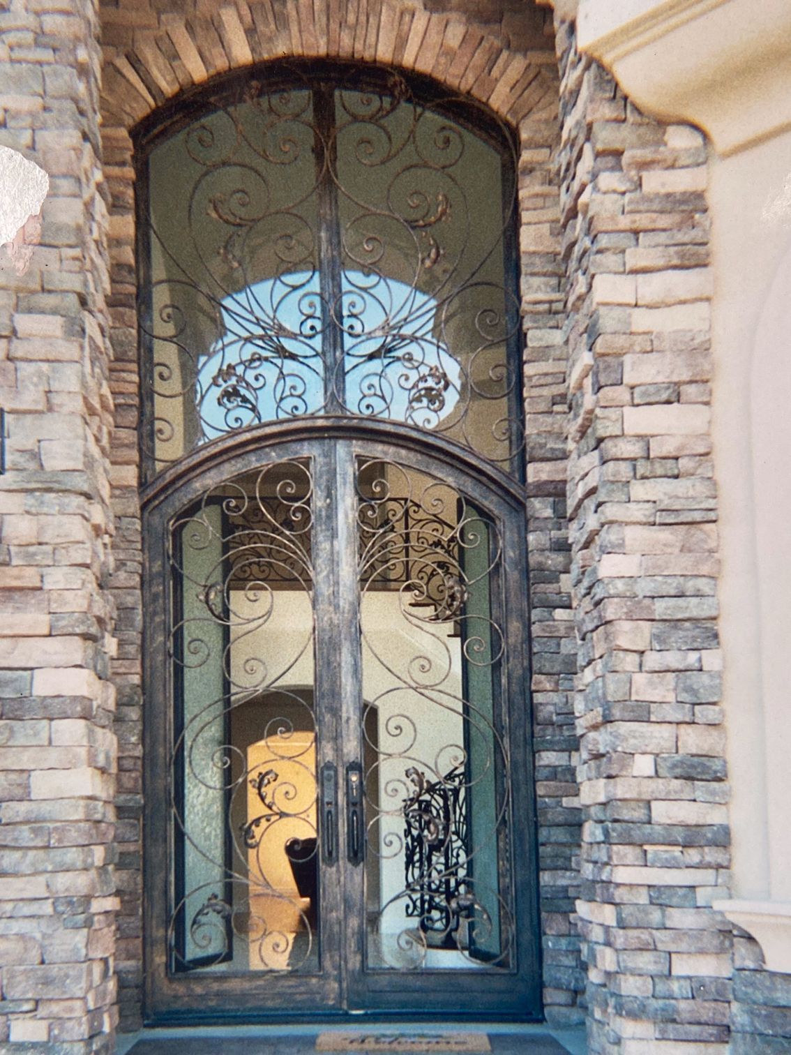 Ornate iron and glass double doors with arched top, set in a stone facade.