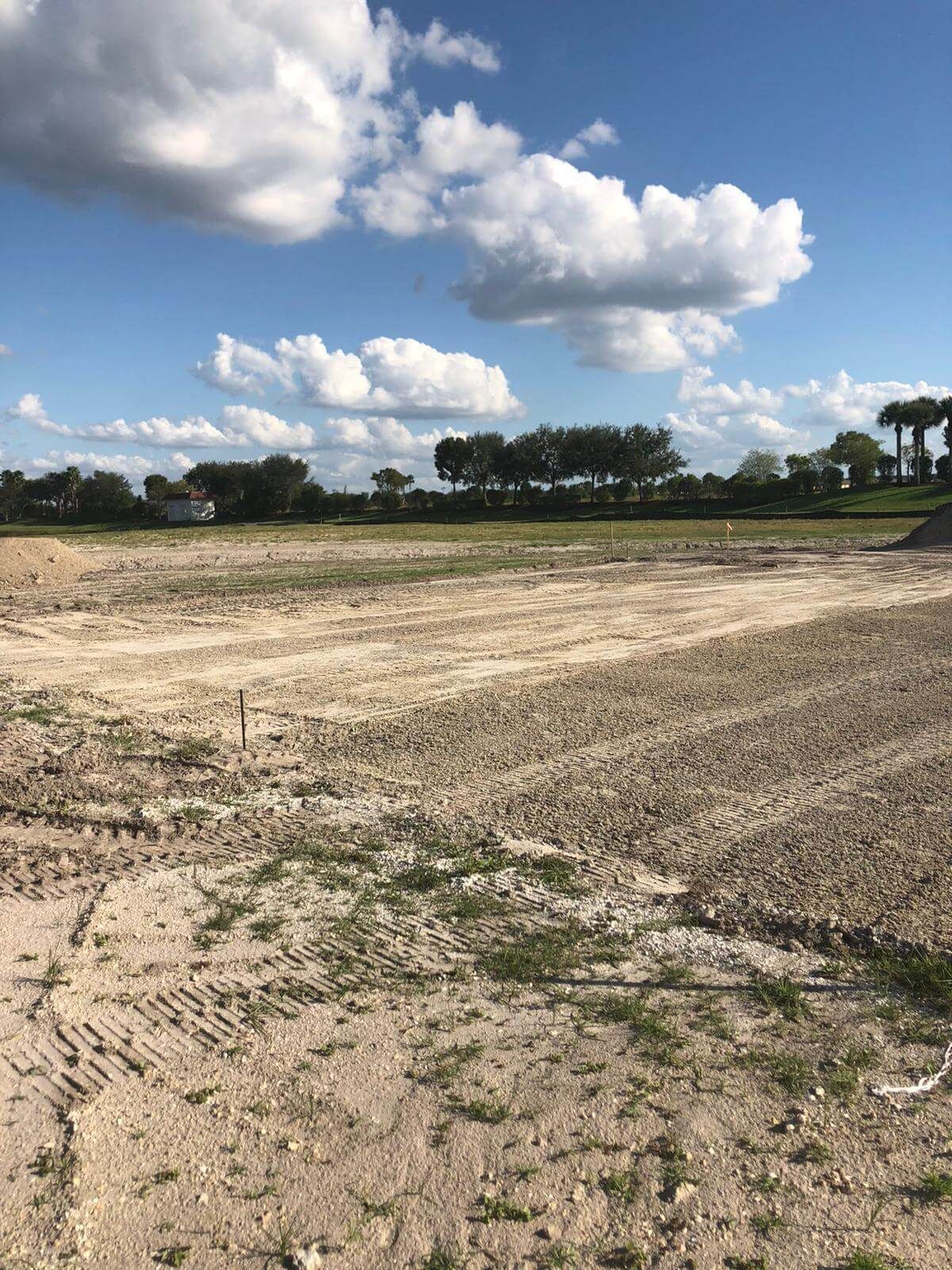 a large dirt field with trees in the background and clouds in the sky.
