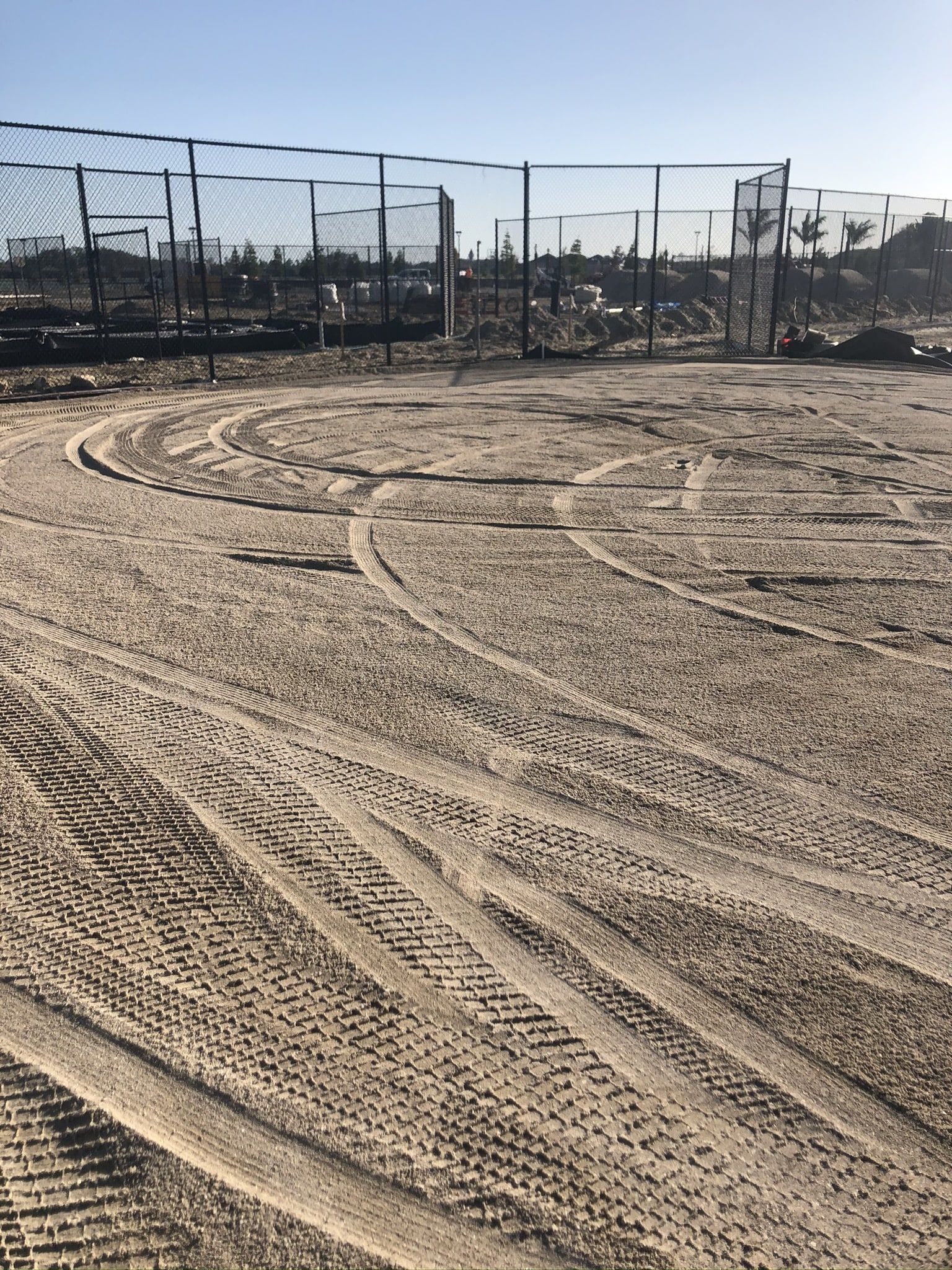 a dirt field with tire tracks and a fence in the background.