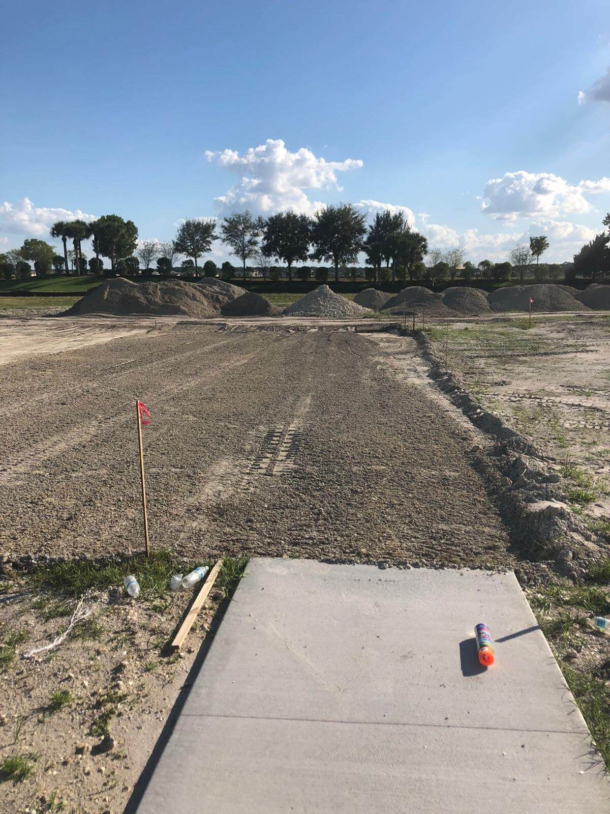 a concrete walkway leading to a dirt field with trees in the background.