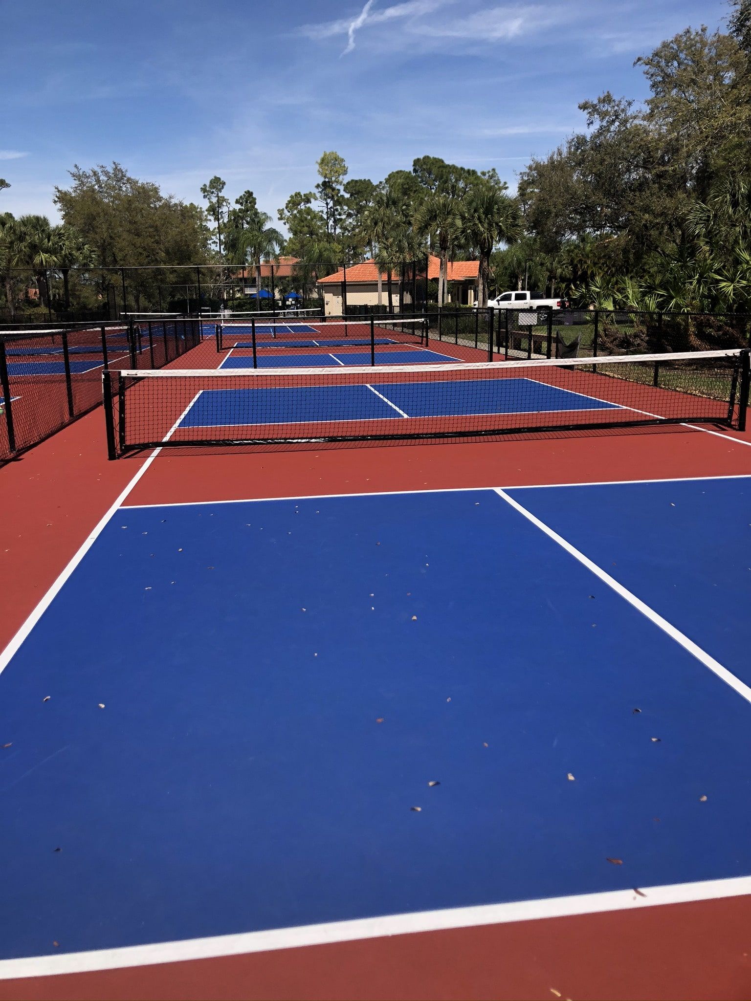 a blue and red tennis court with a fence and trees in the background.