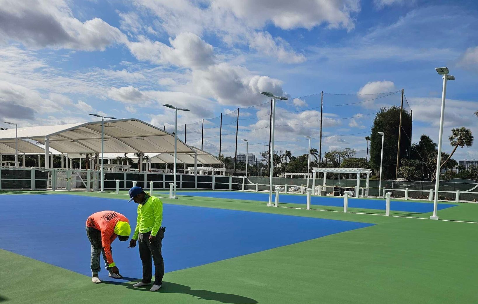 Two men are working on a tennis court on a sunny day.