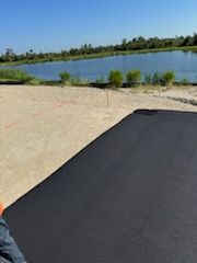 A person is sitting on a black blanket in front of a lake.