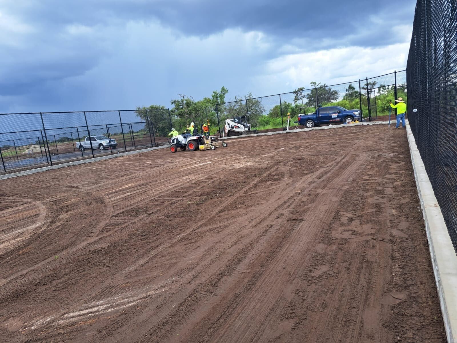 a group of people are working on a dirt field next to a fence.