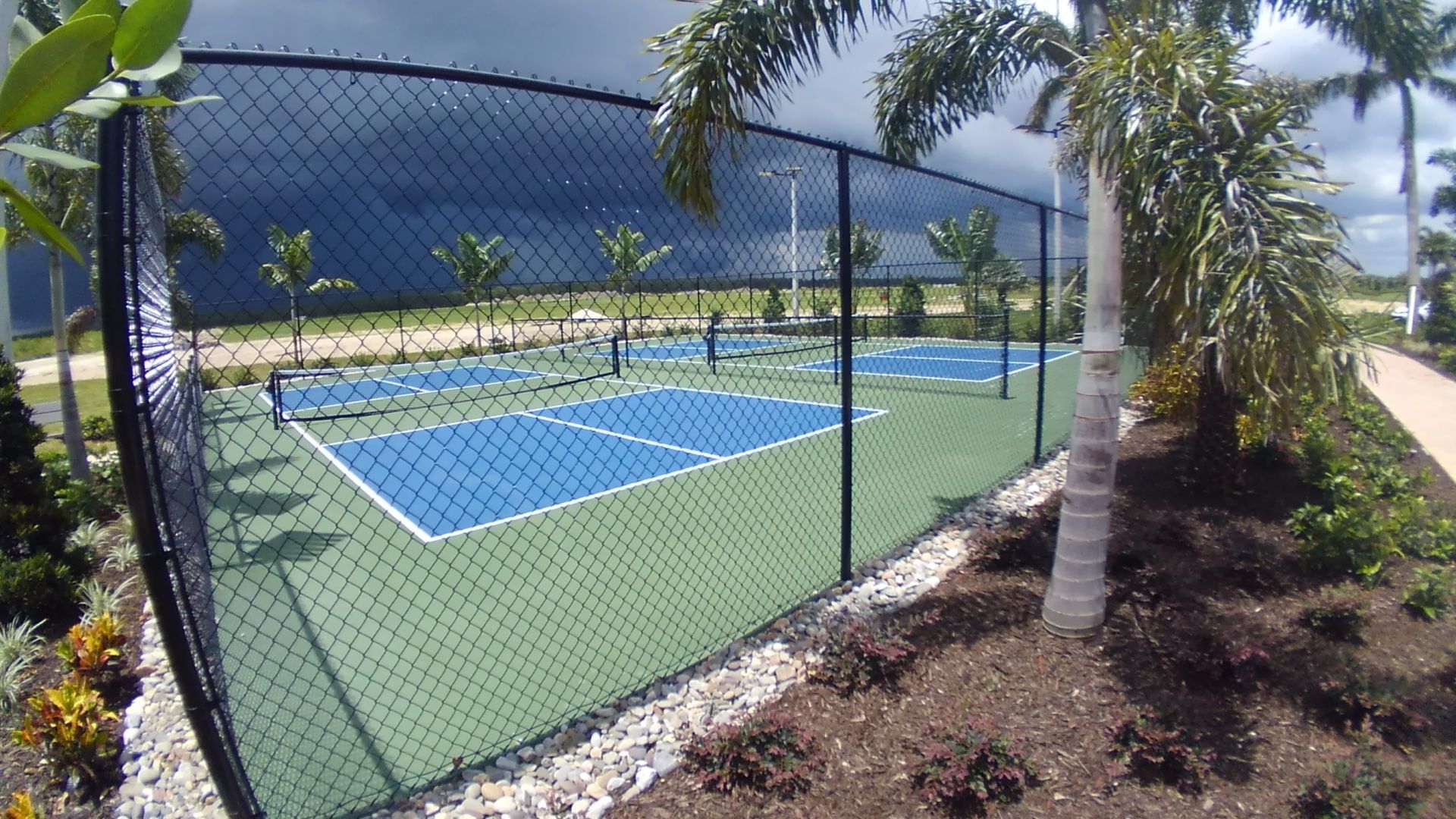 a tennis court behind a chain link fence with palm trees in the background