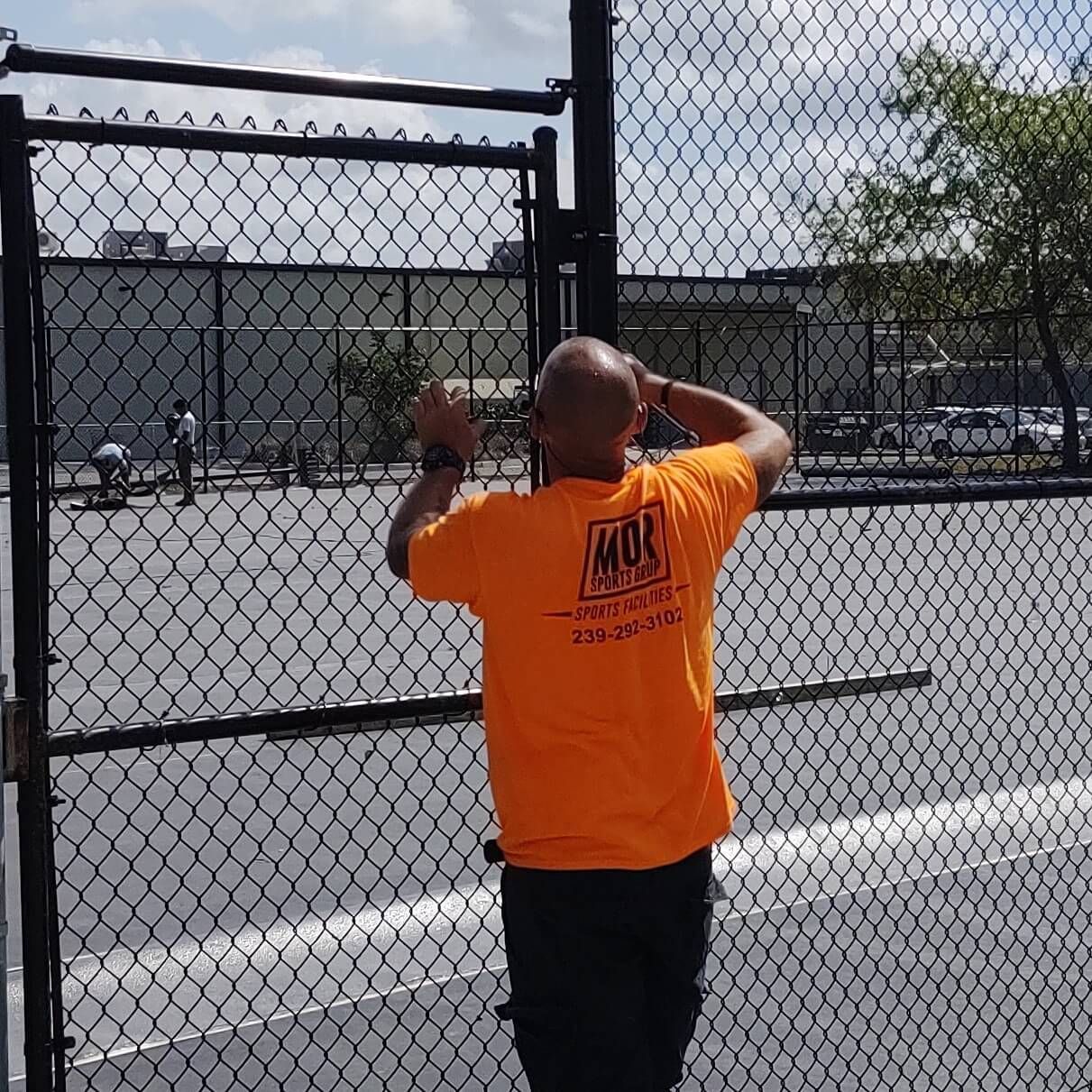 a man in an orange shirt is standing in front of a chain link fence.
