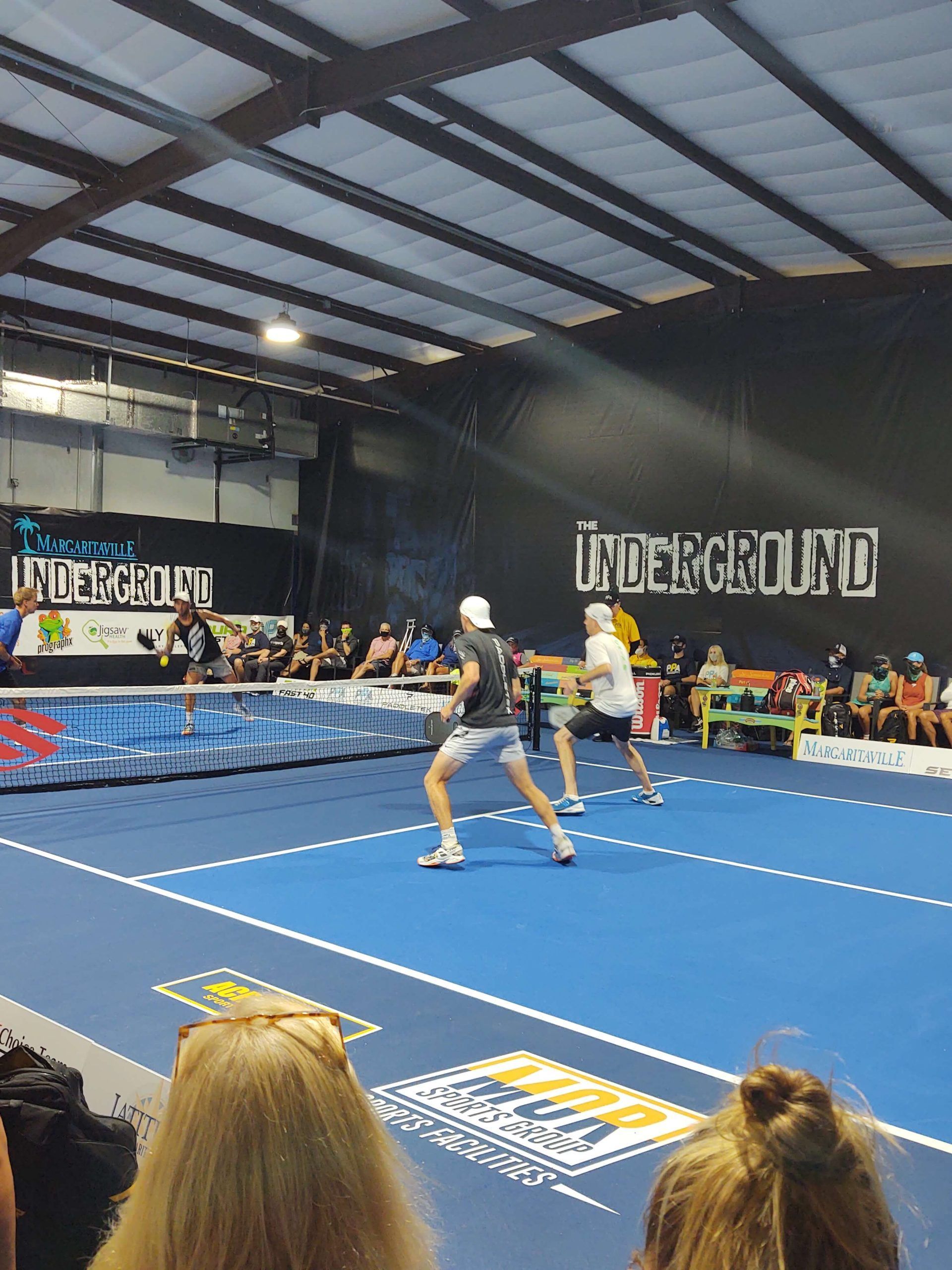 a group of people are watching a tennis match in an indoor court.
