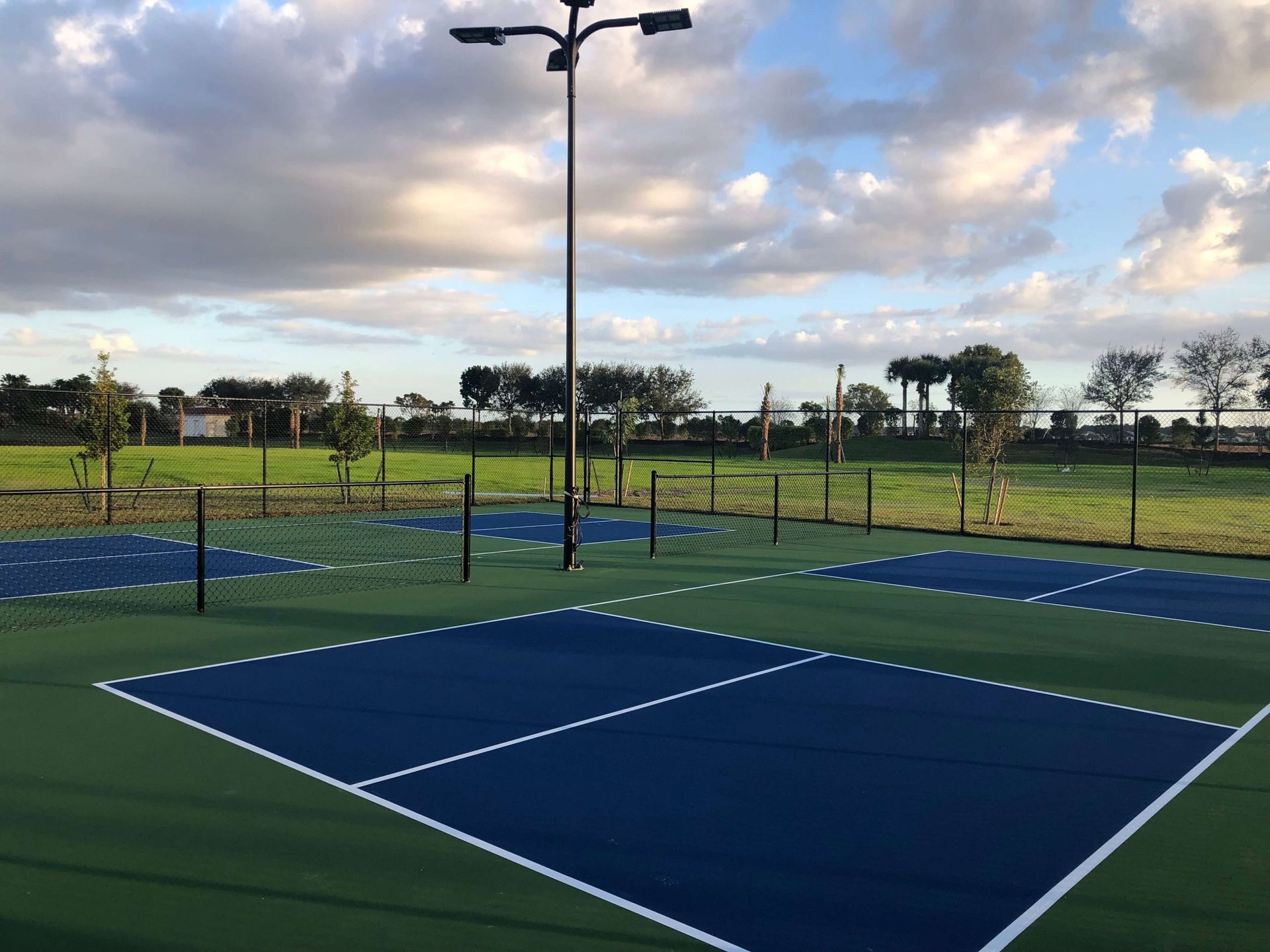 a tennis court with a fence and lights on a cloudy day.