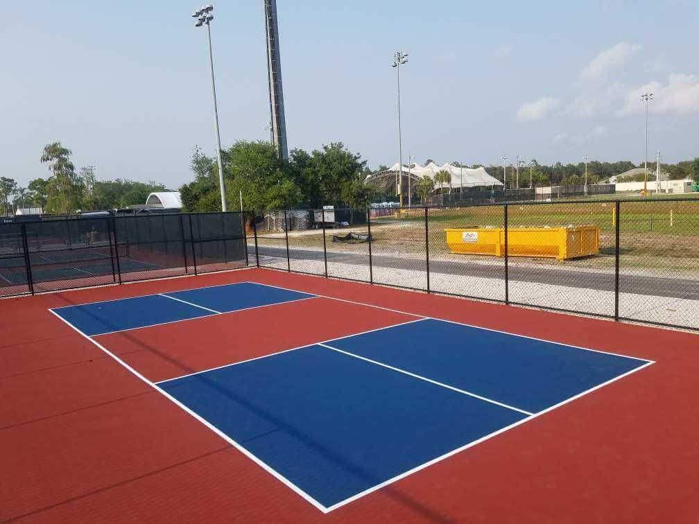 a blue and red tennis court with a yellow dumpster in the background