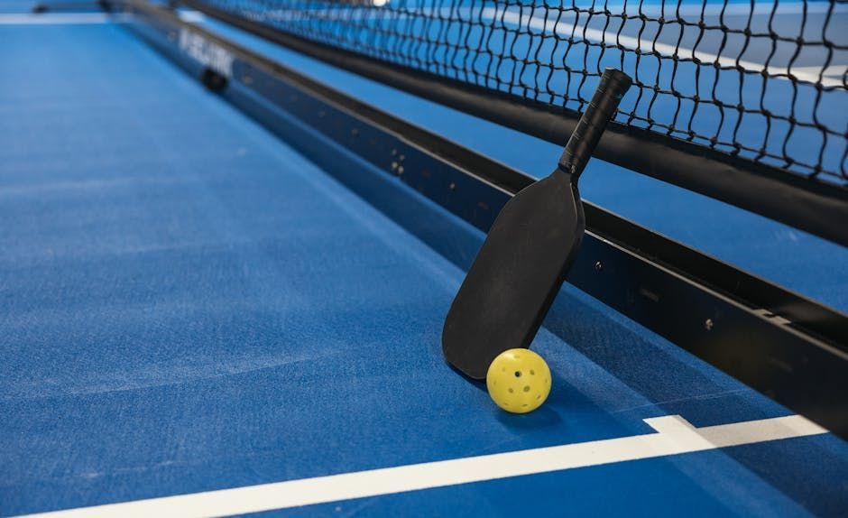 Pickleball paddle and ball on a blue court next to a net.