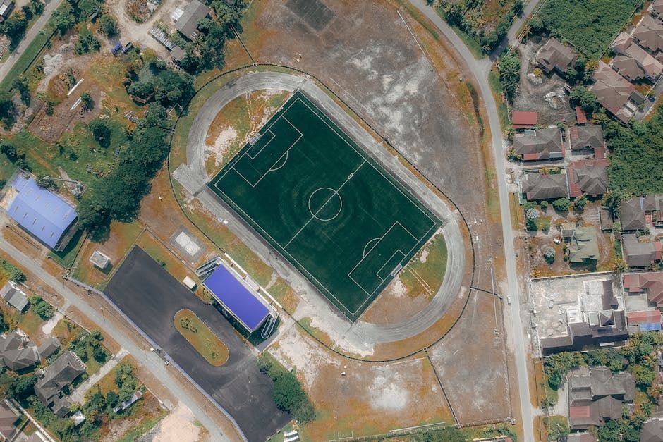 Aerial view of a soccer field with a running track, surrounded by houses and trees.