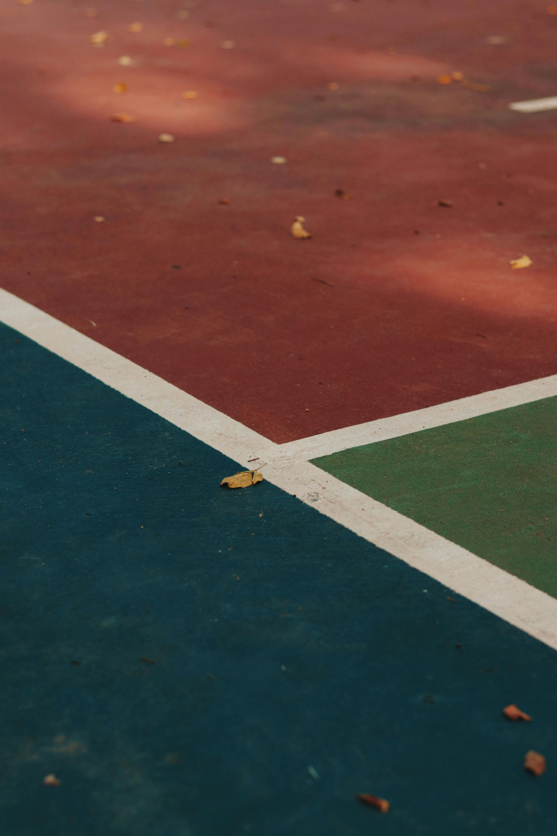 A close up of a basketball court with leaves on the ground.