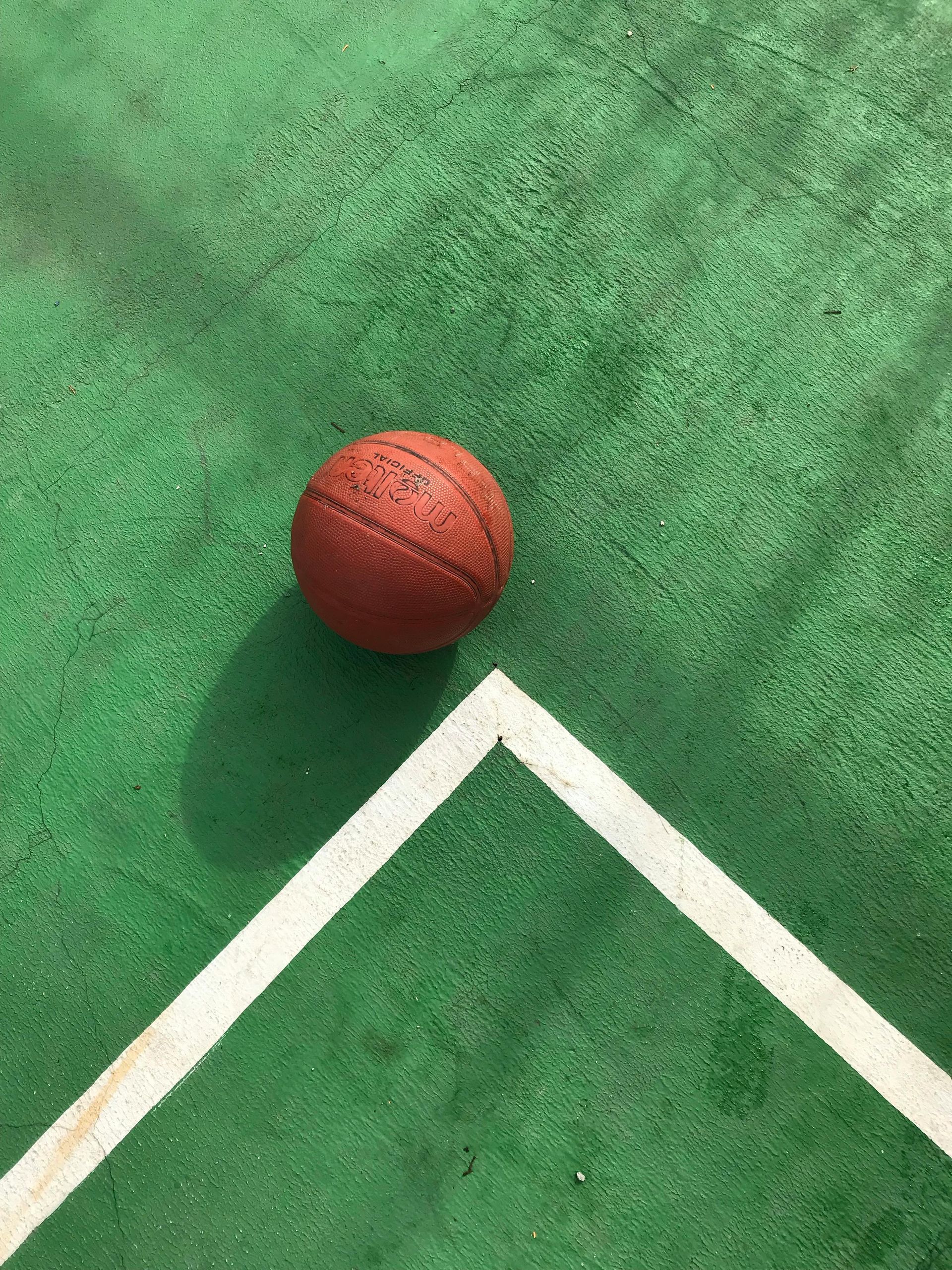 A basketball is sitting on a green court next to a white line.