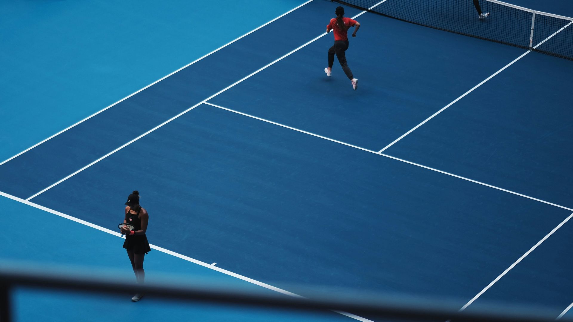 Two people are playing tennis on a blue court.