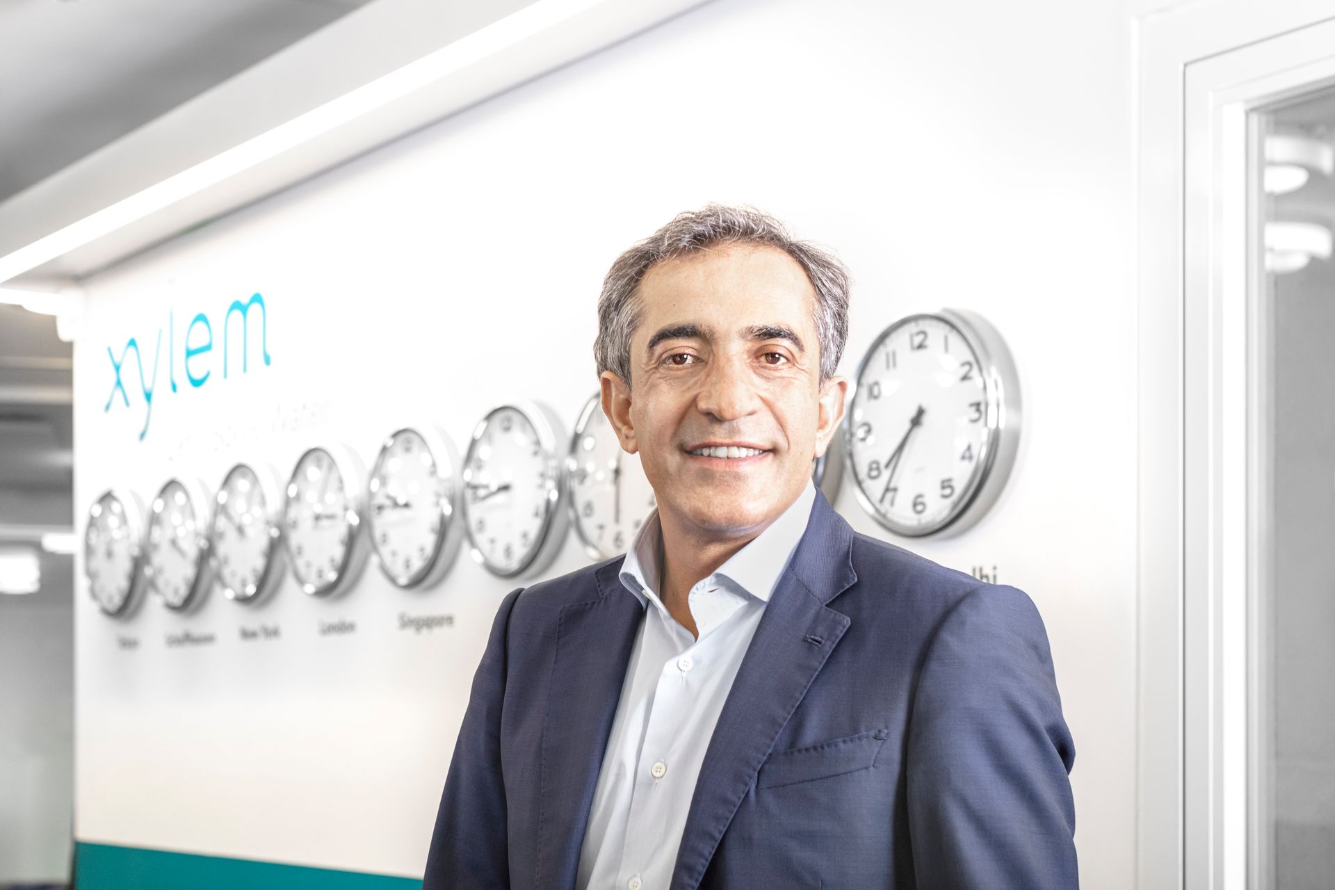 A man in a suit is standing in front of a wall with clocks on it.