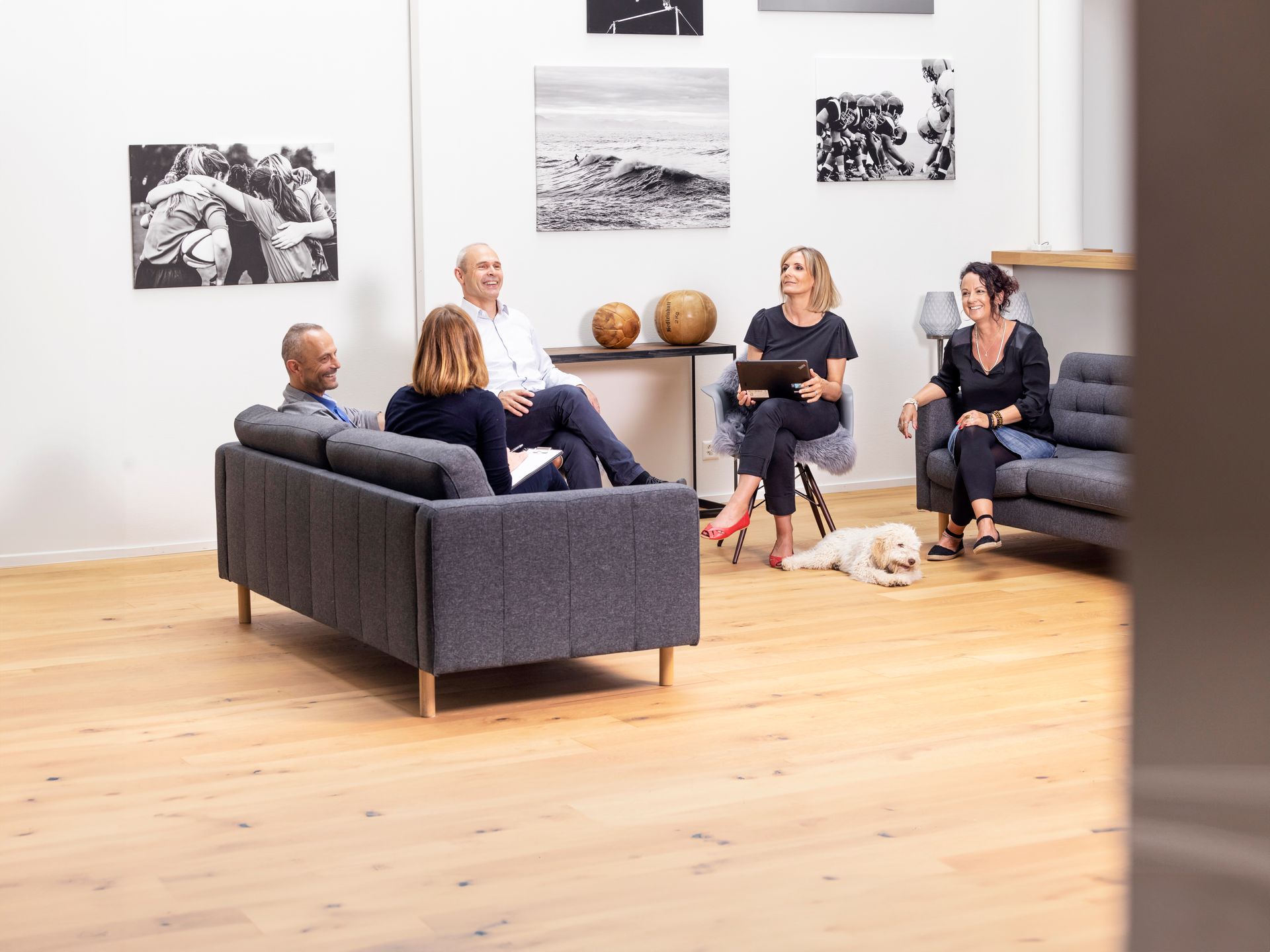 Eine Gruppe von Menschen sitzt mit einem Hund auf einem Sofa in einem Bürogebäude.