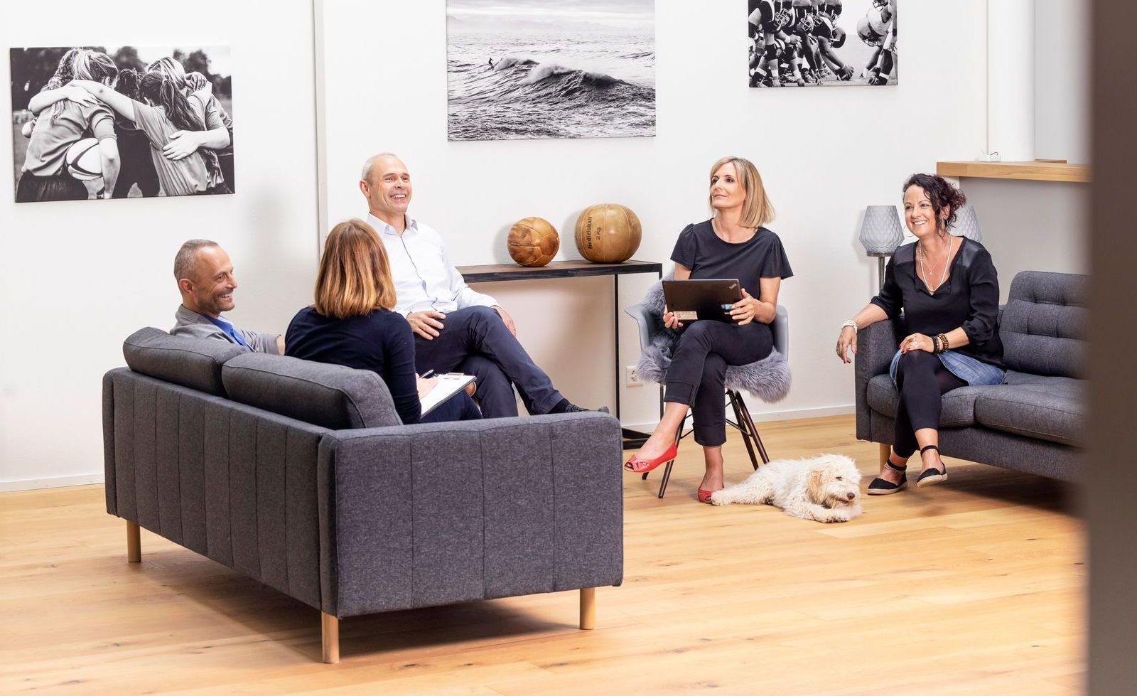 Eine Gruppe von Menschen sitzt mit einem Hund auf Sofas in einem Büro.
