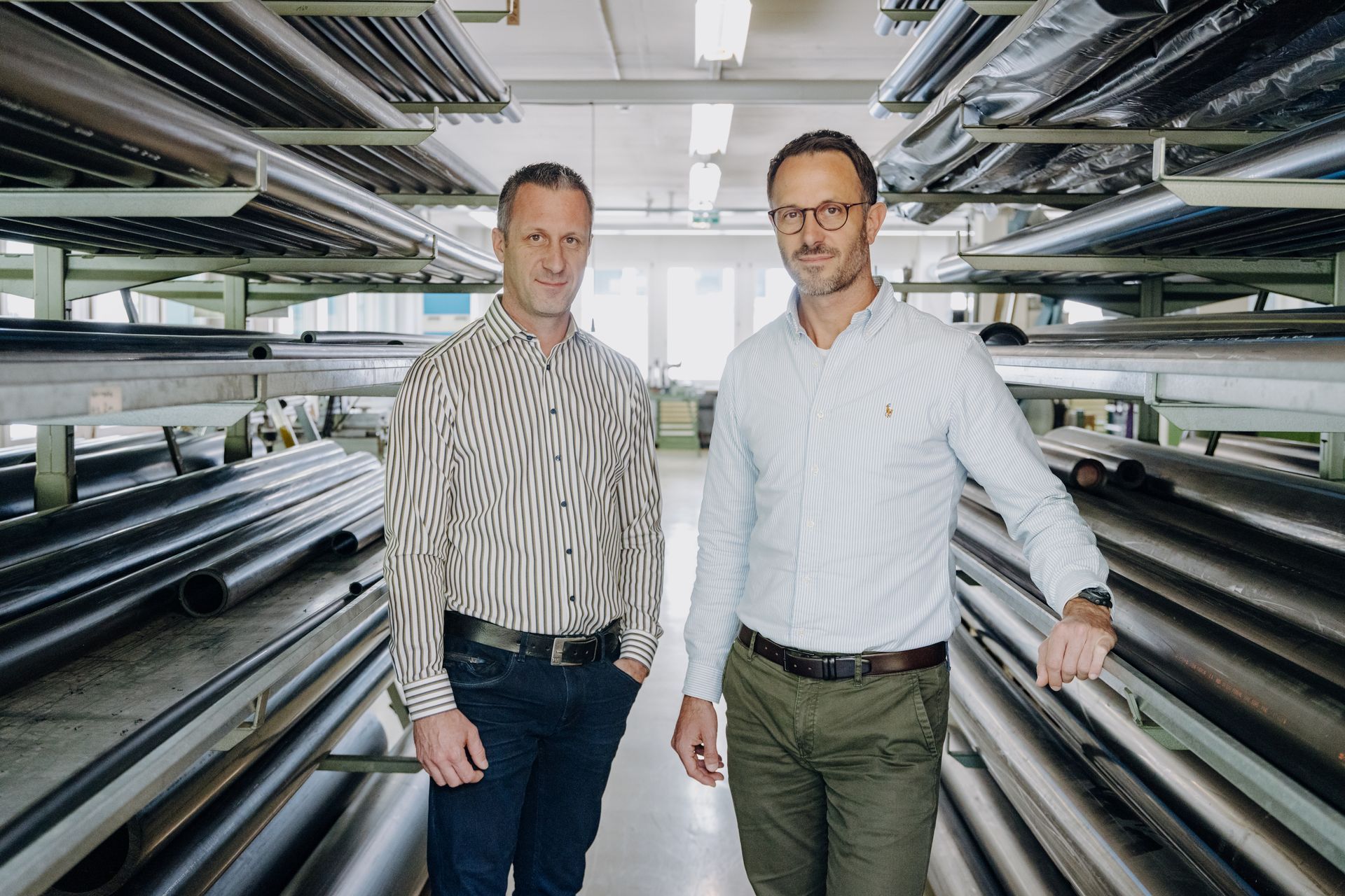 Two men are standing next to each other in a room filled with pipes.