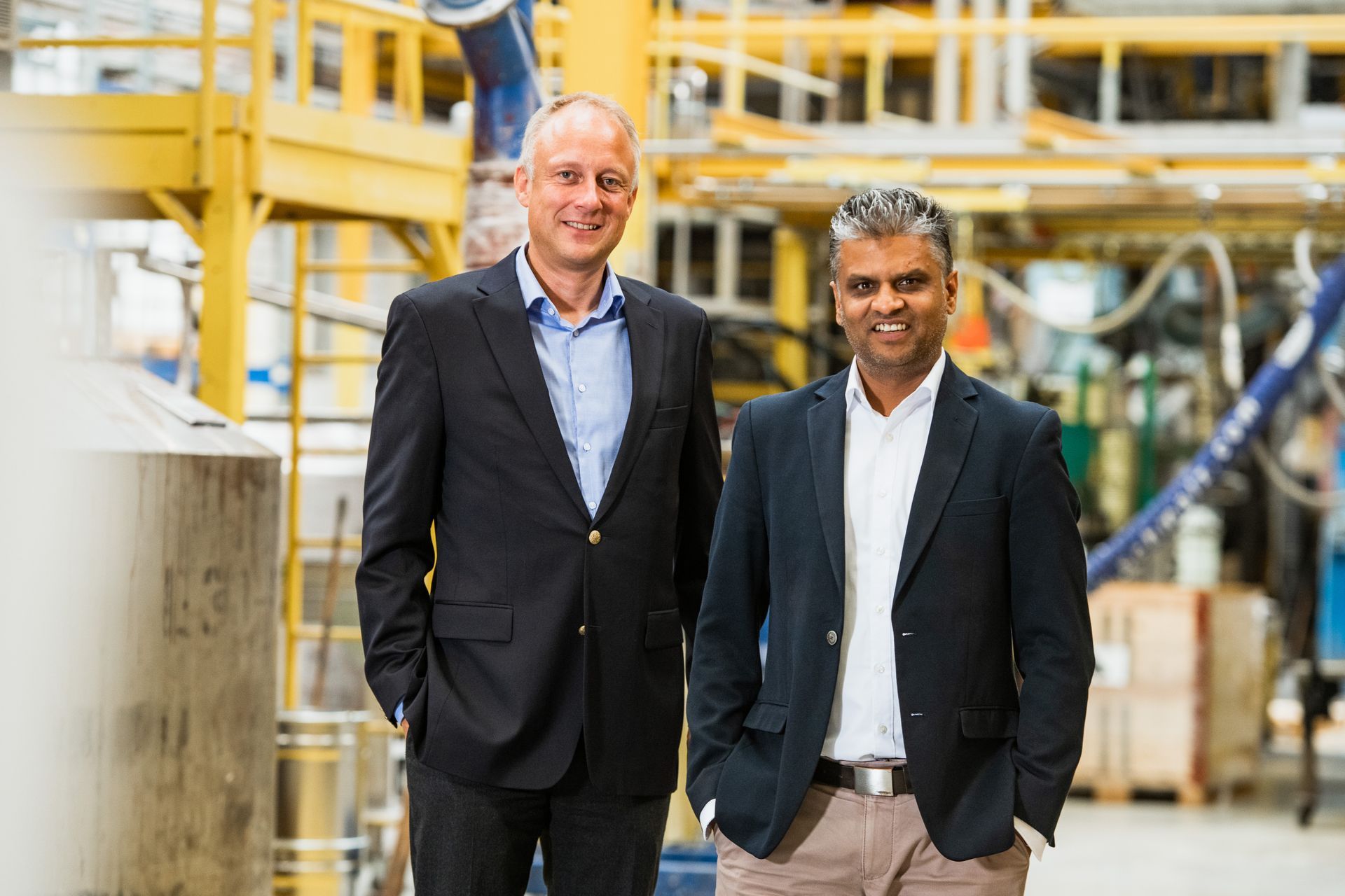 Two men in suits are standing next to each other in a factory.