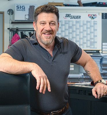 Der Geschäftsführer von SIG Sauer steht in seinem Büro vor einer Wand mit den Produkten von SIG Sauer