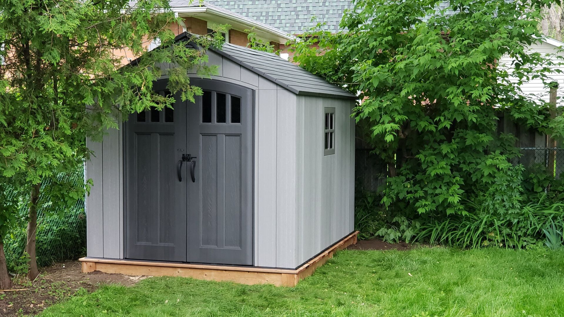 Small wooden shed nestled in a lush green yard with a neatly mowed lawn.