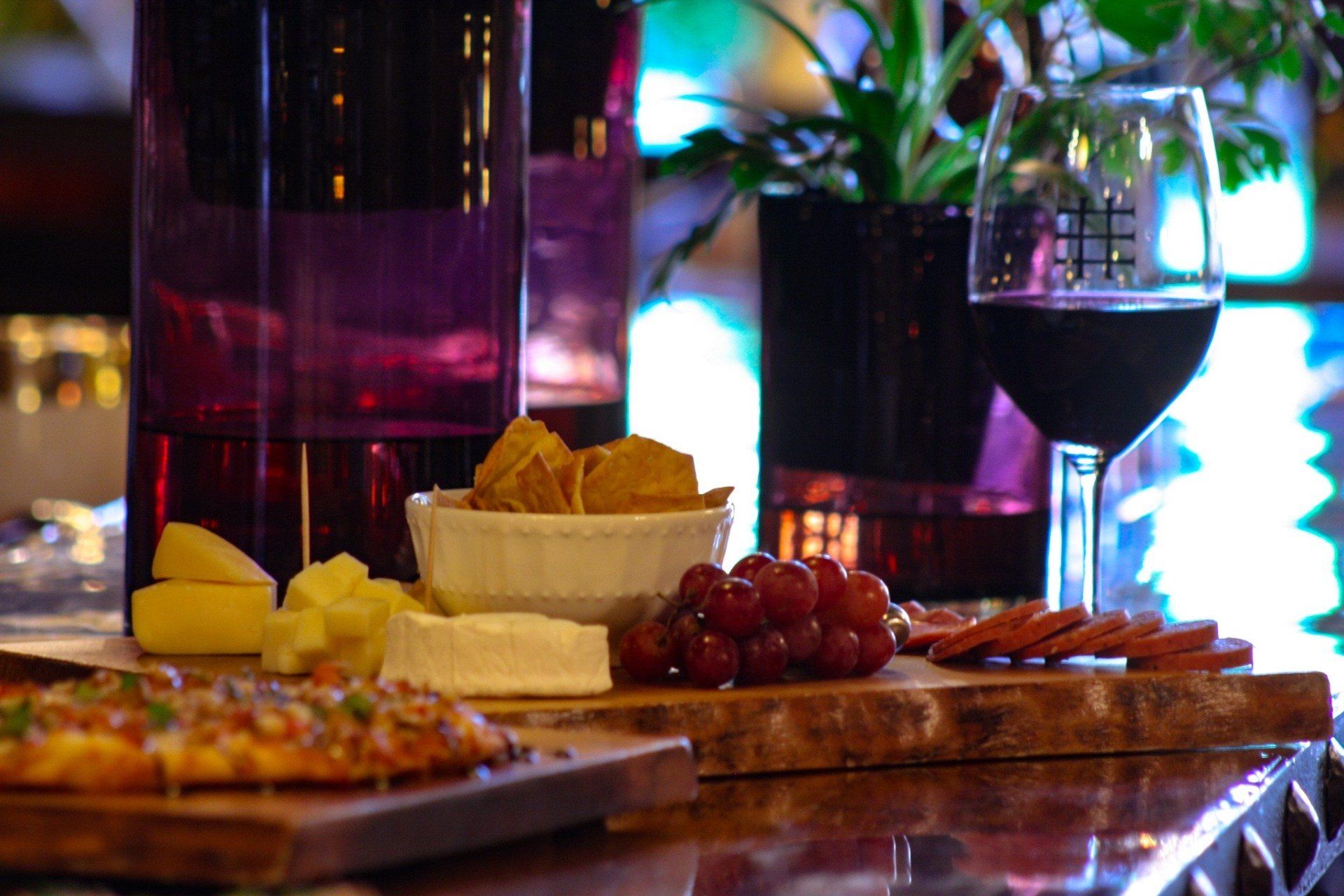 A cutting board with cheese , grapes , and a glass of wine on a bar.