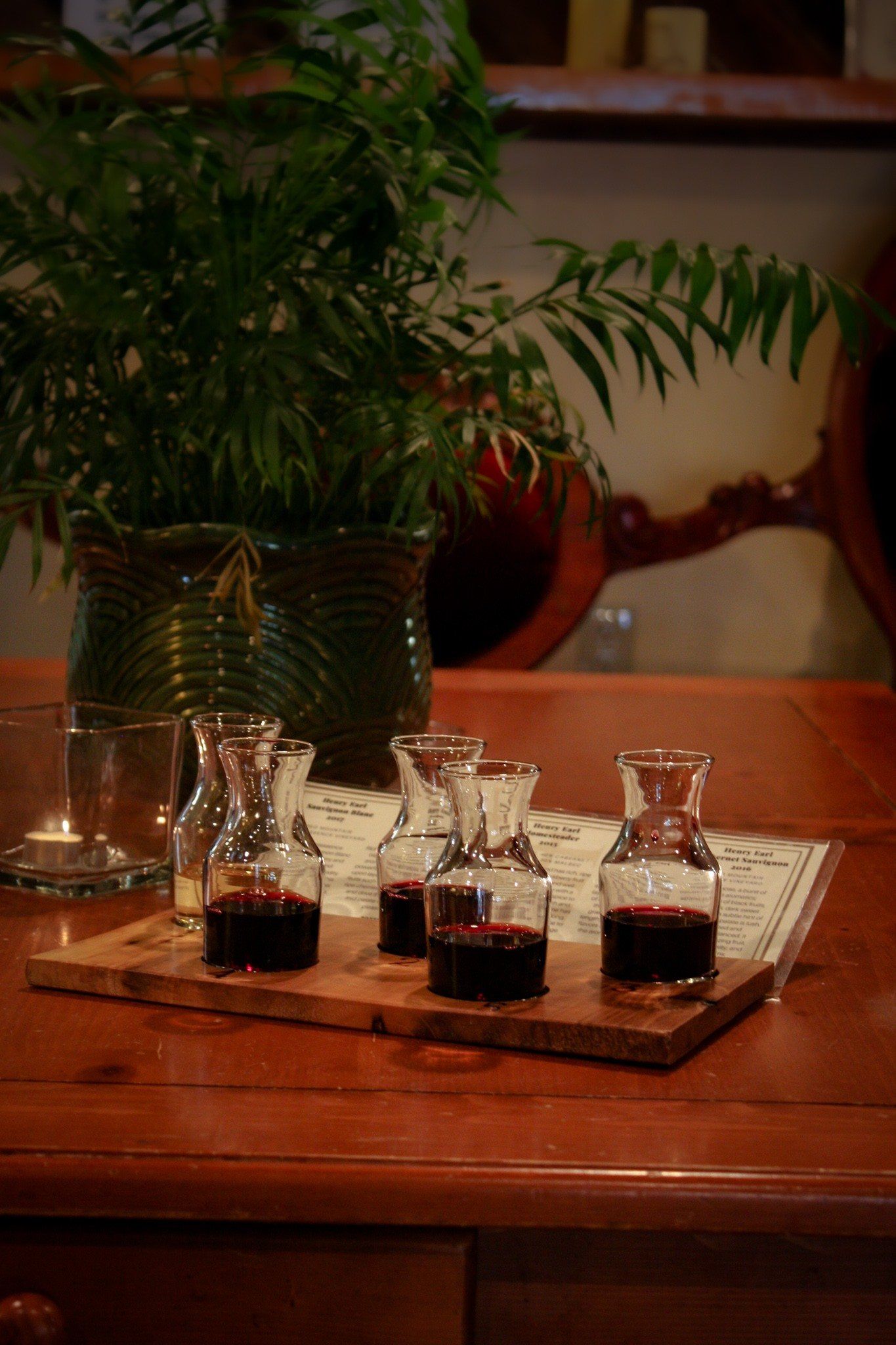 A wooden table topped with a tray of shot glasses and bottles of wine.