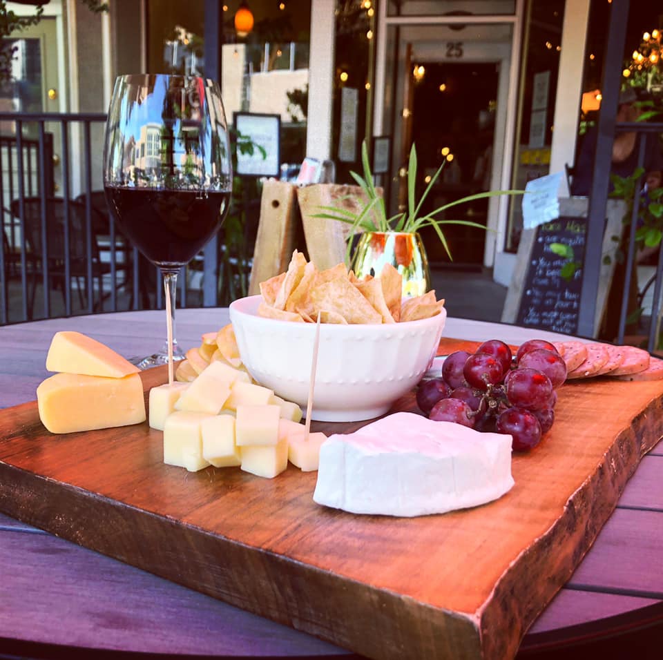 A wooden cutting board with cheese grapes and chips on it