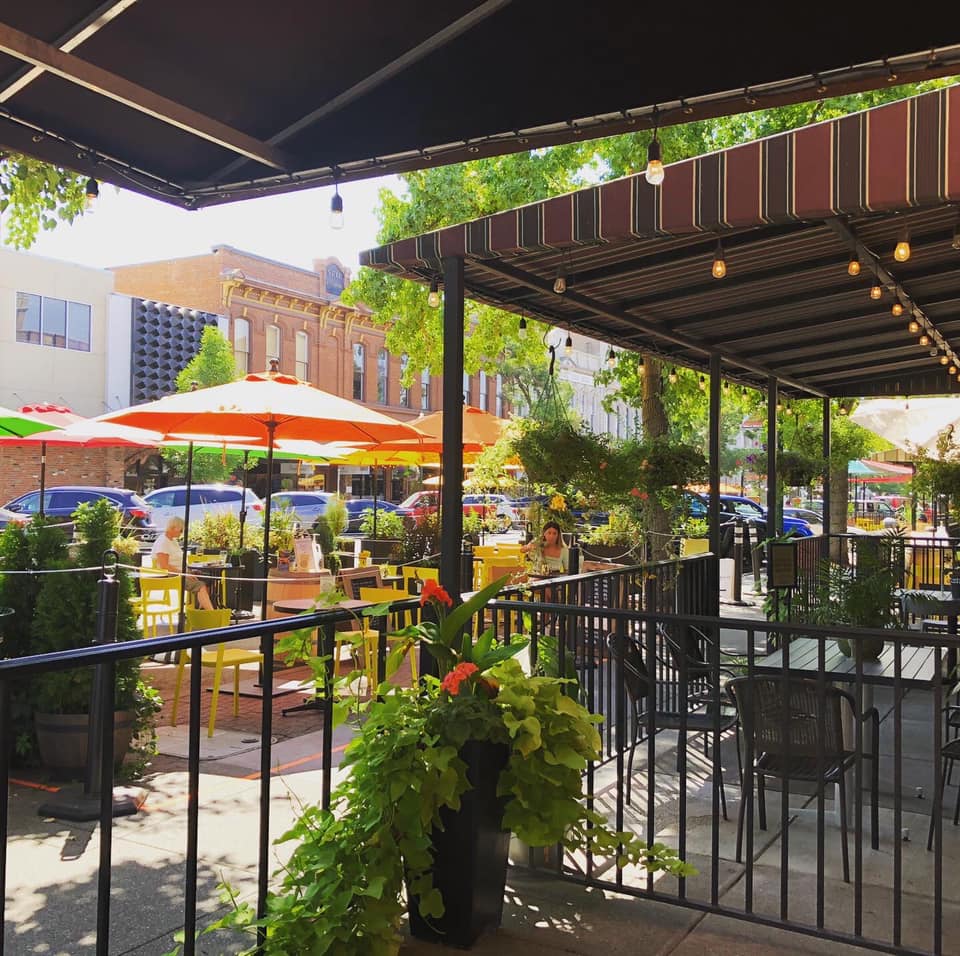 A patio with tables , chairs , umbrellas and potted plants.