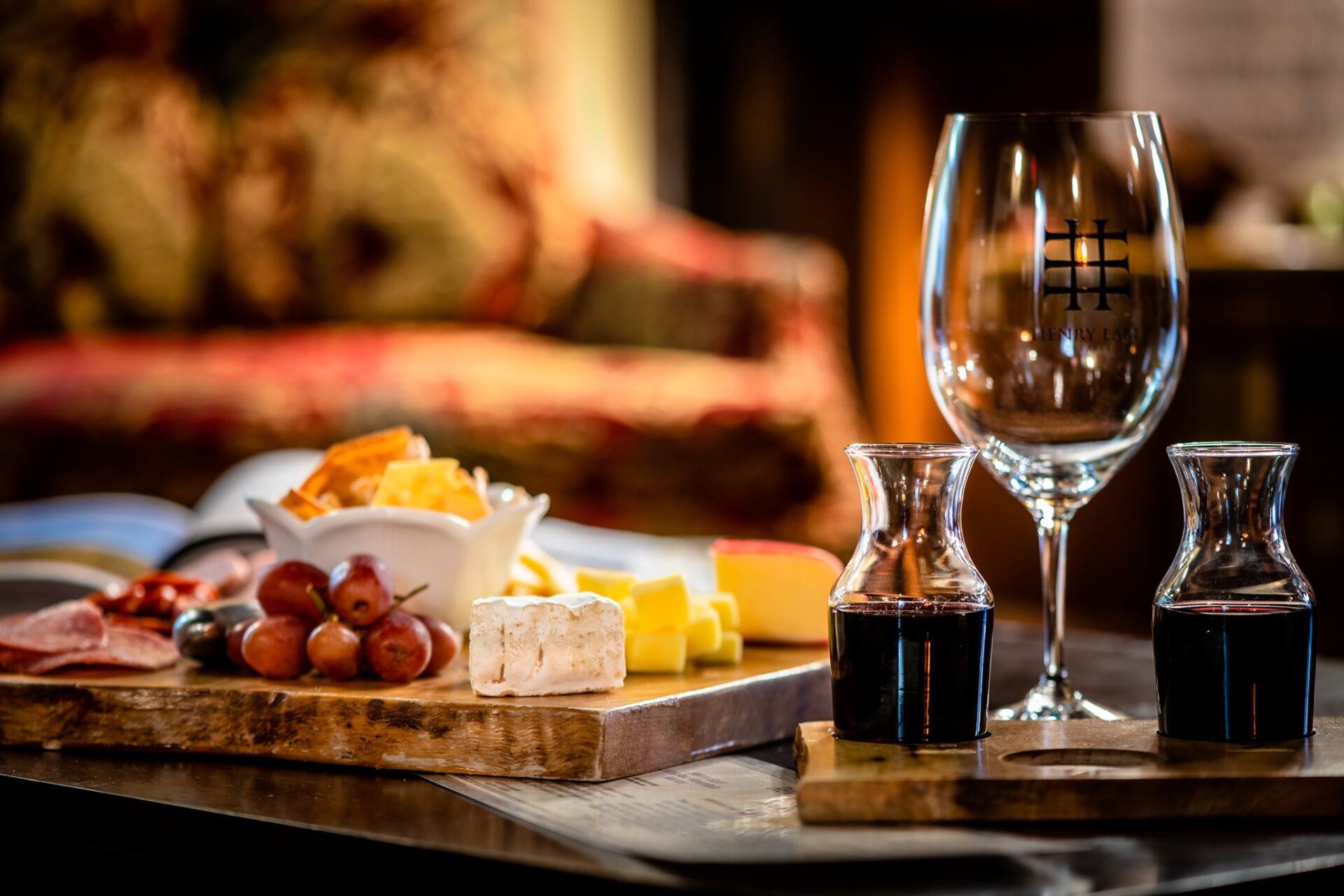 A wooden cutting board with a variety of food and wine glasses on it.