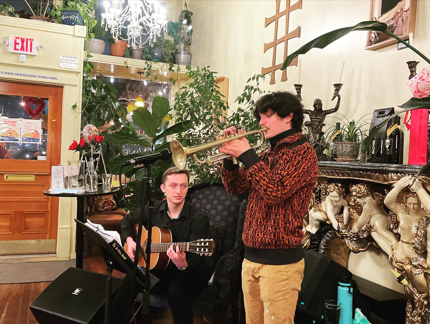 A man is playing a trumpet while another man plays a guitar.