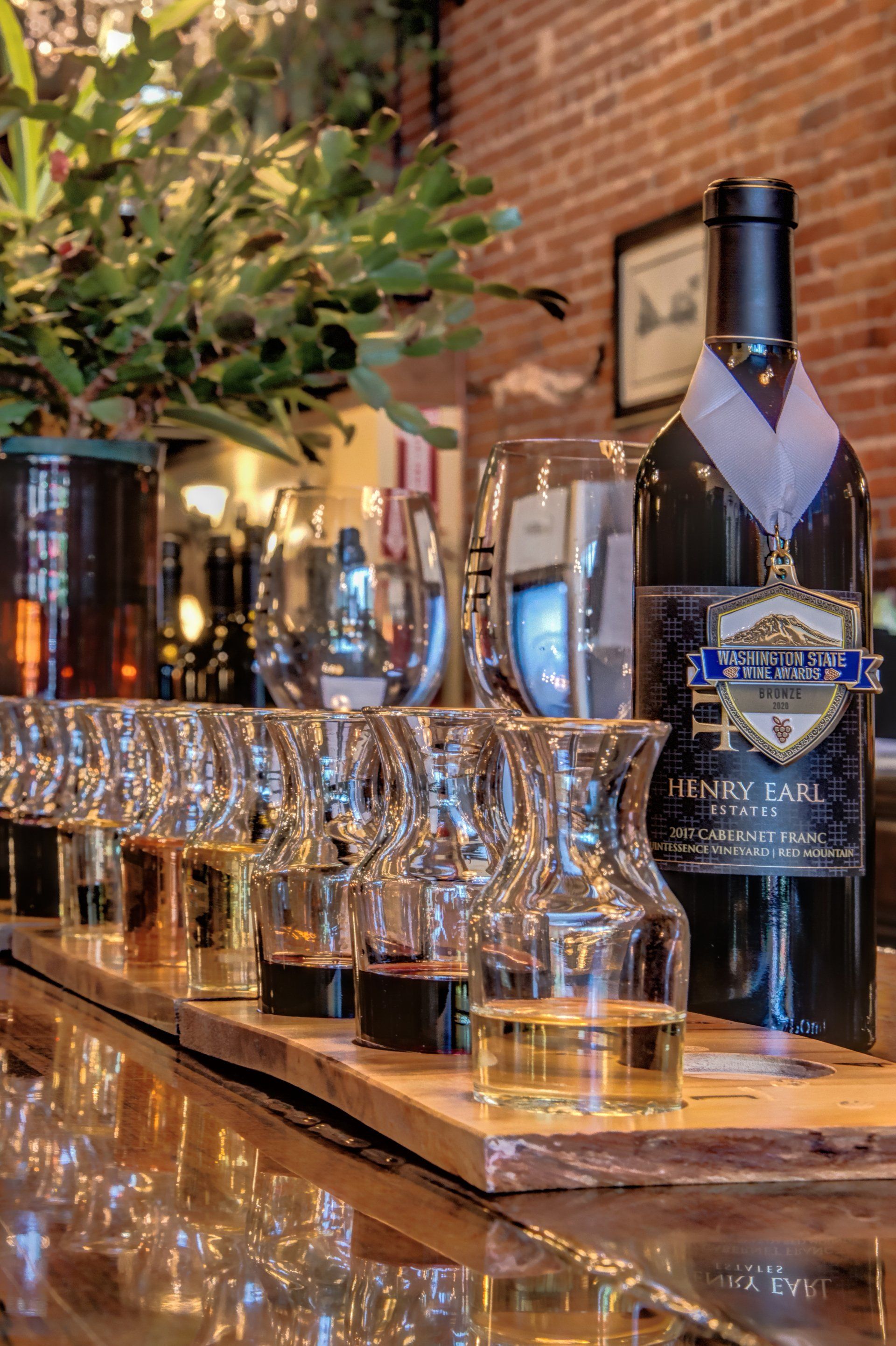 A bottle of wine is sitting on a bar next to a row of wine glasses.