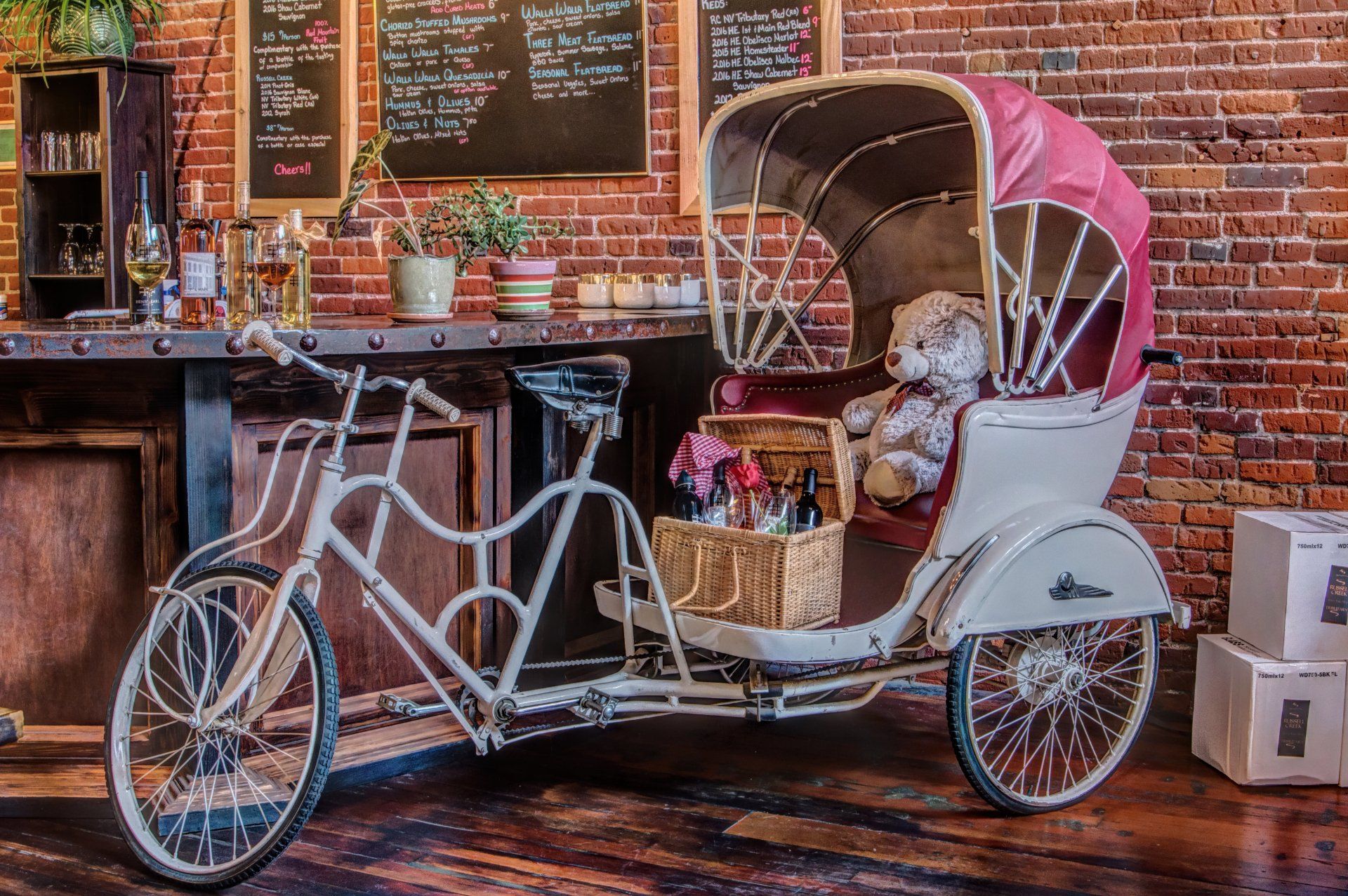 A rickshaw with a teddy bear in it is parked in front of a brick wall.